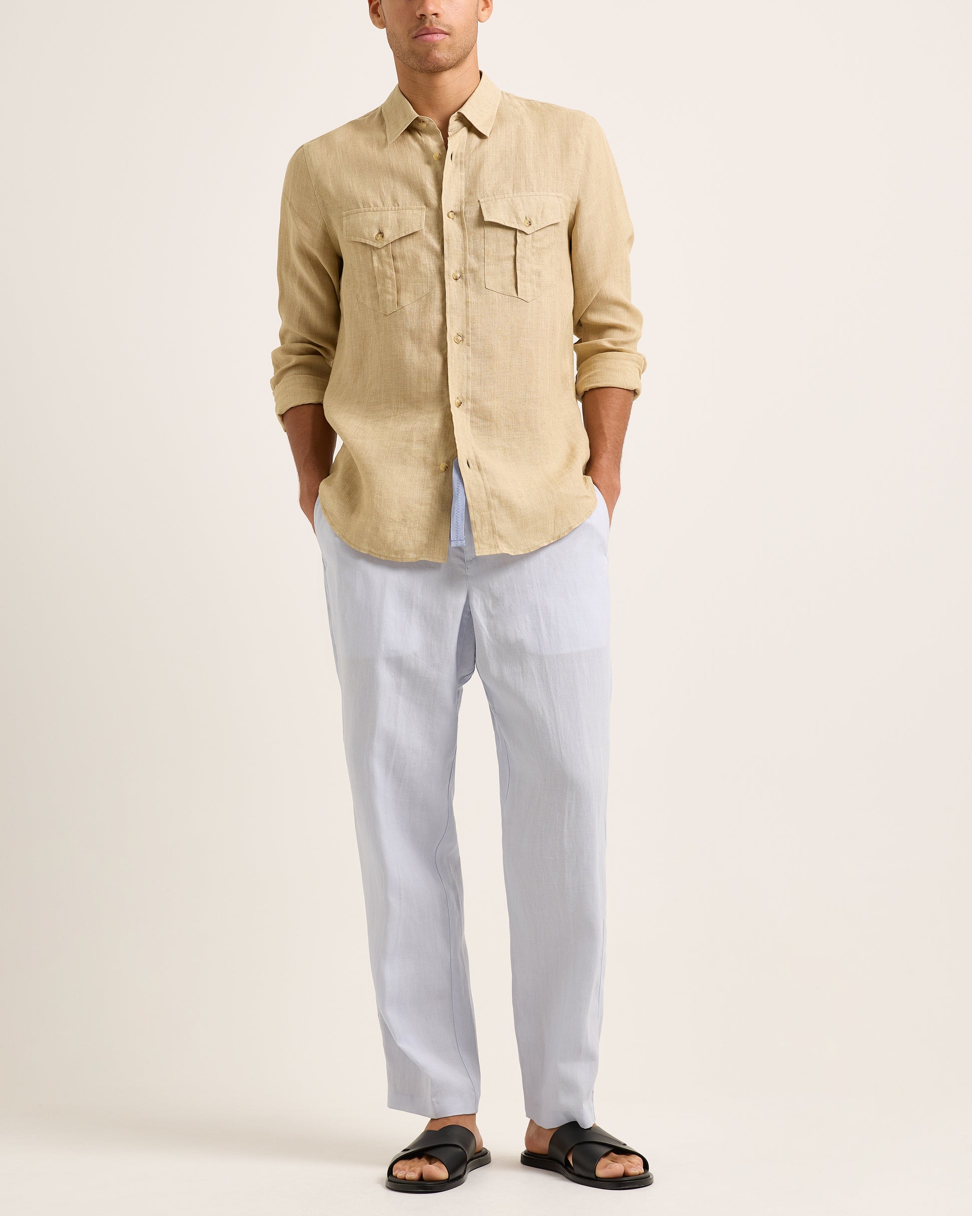 Person wearing a beige shirt and light blue trousers with a blue drawstring on a white background