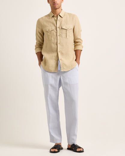 Person wearing a beige shirt and light blue trousers with a blue drawstring on a white background