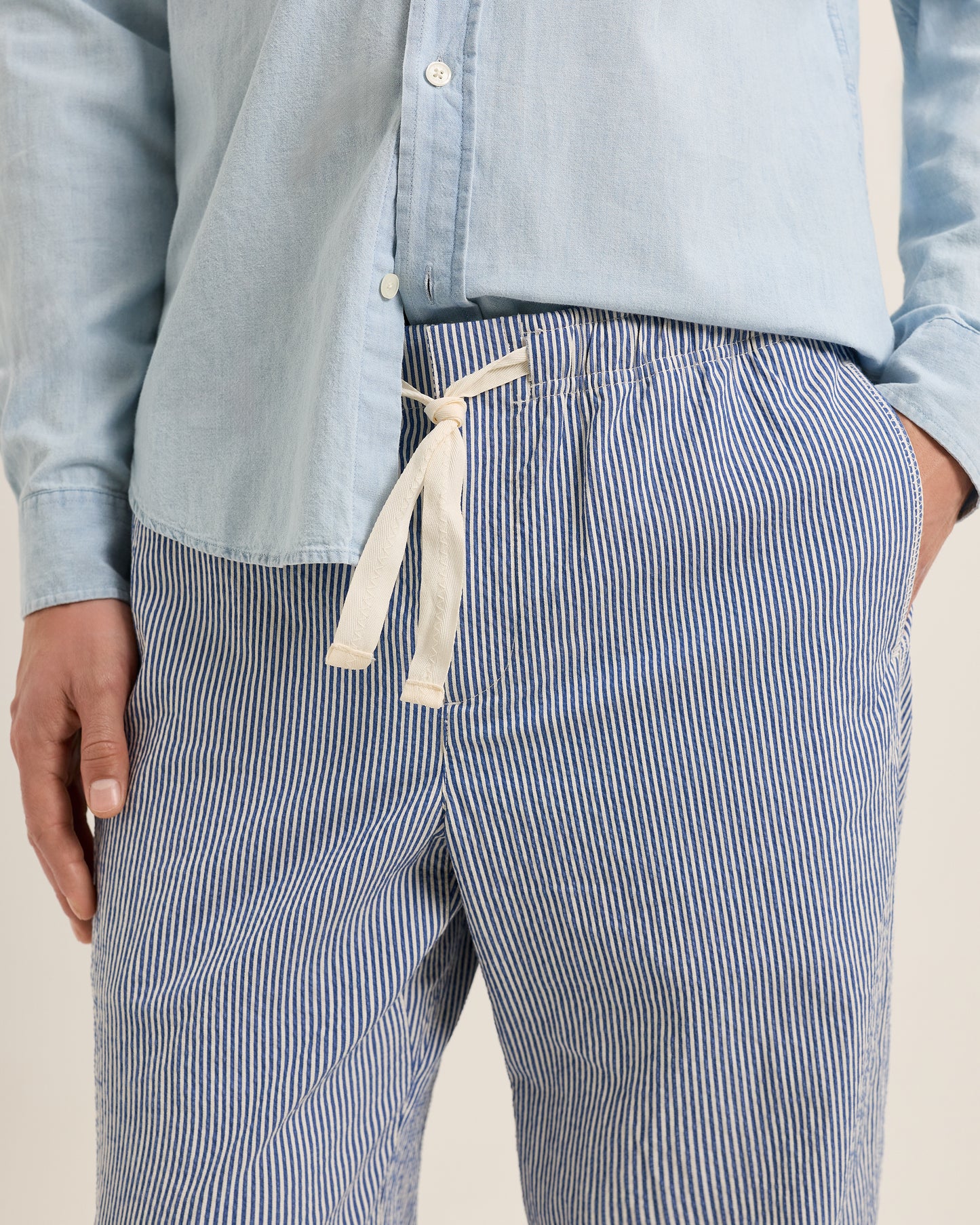 Person wearing a light blue shirt and blue striped pants on a neutral background