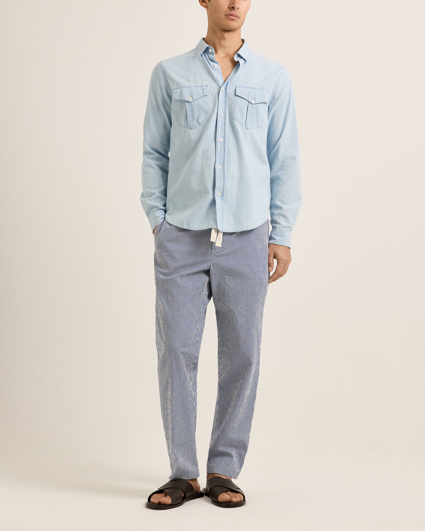 Person wearing a light blue denim shirt and gray pants on a beige background