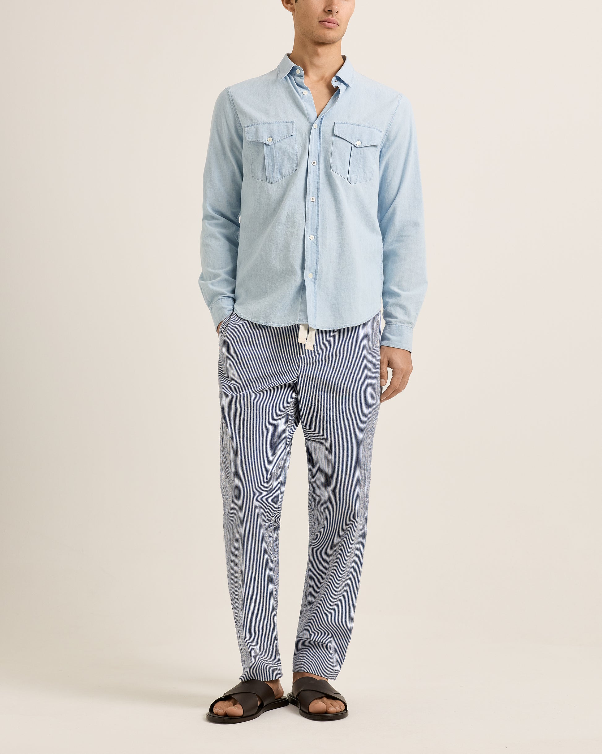 Person wearing a light blue denim shirt and gray pants on a beige background