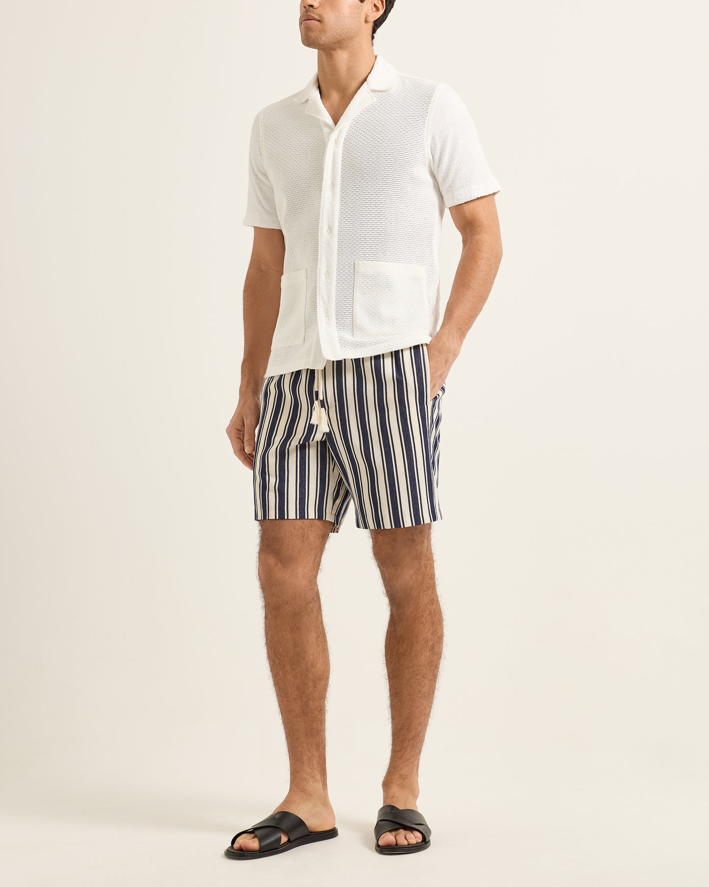Man wearing a white shirt and striped shorts on a plain background