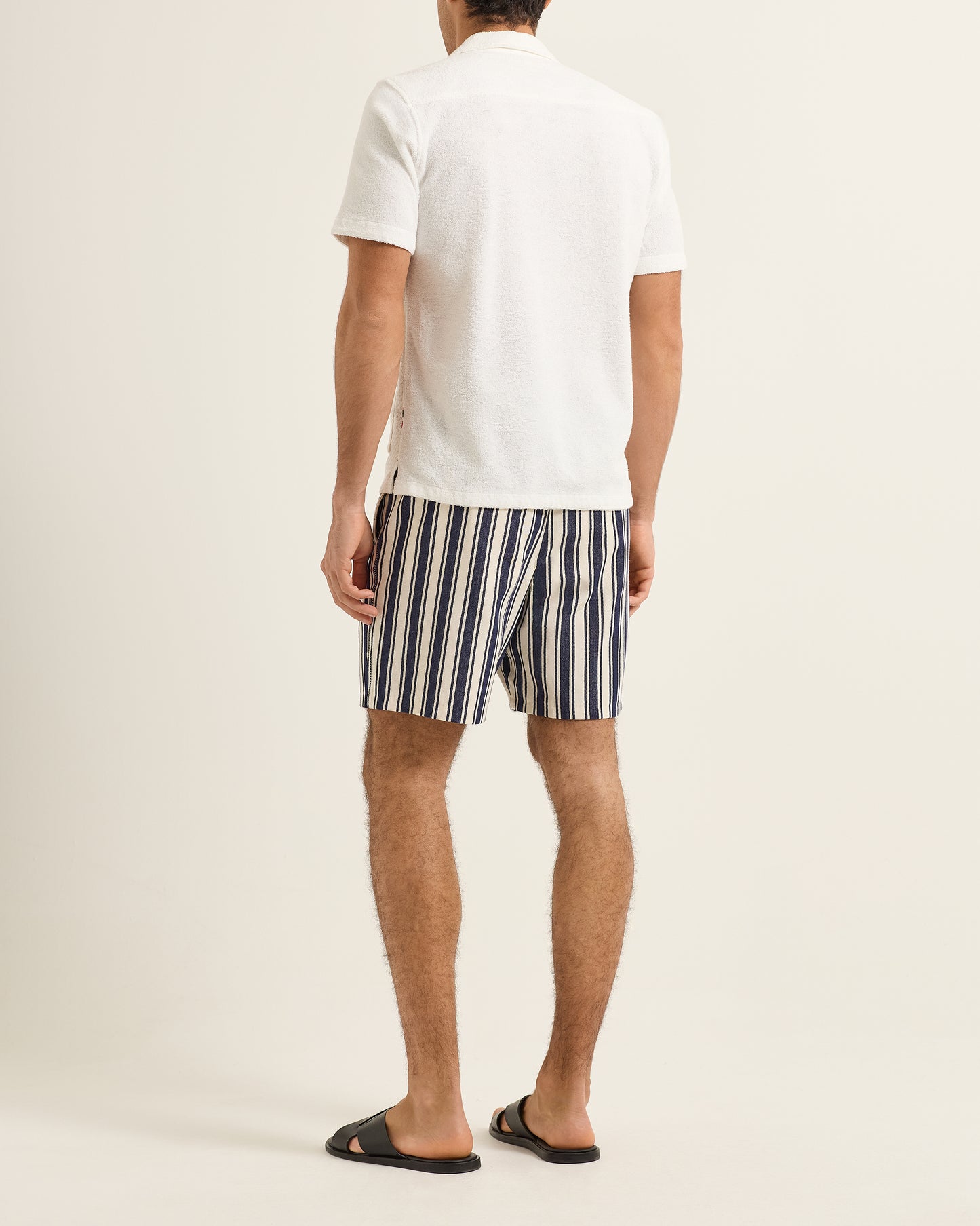 Person wearing a white polo shirt and striped shorts on a plain background