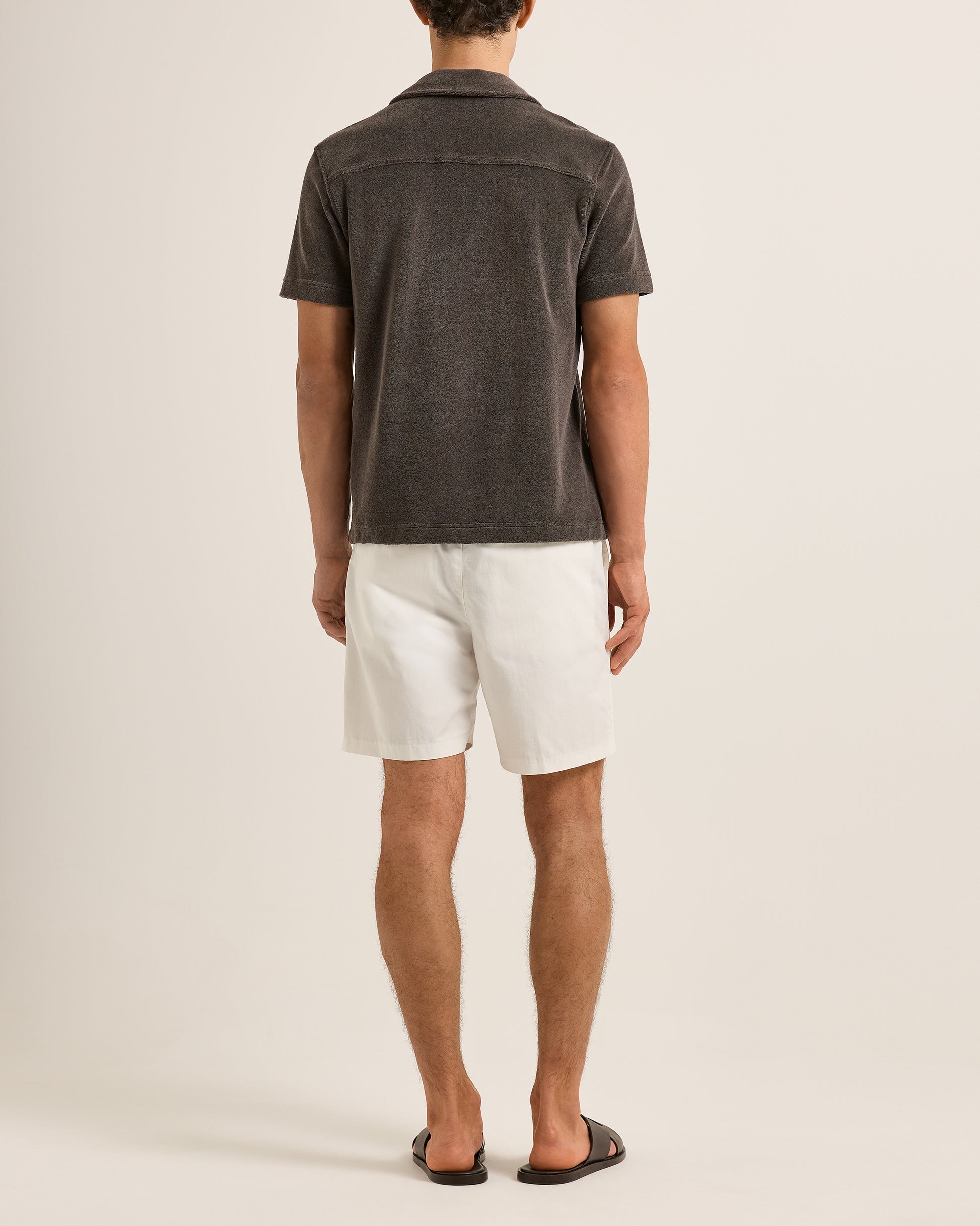 Person wearing a dark gray shirt and white shorts on a plain background