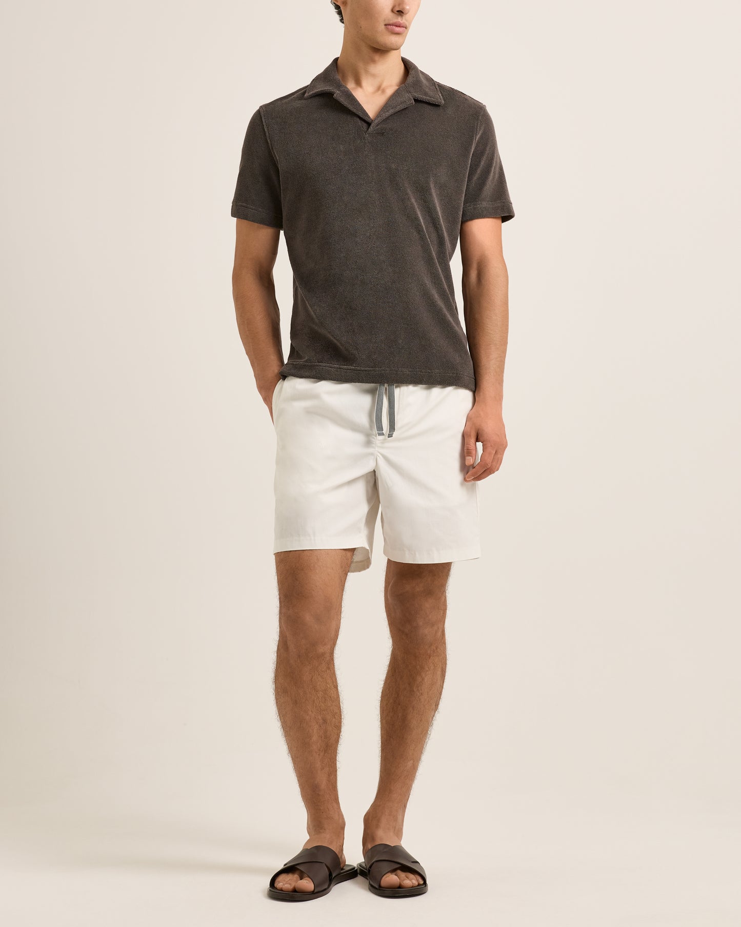 Man wearing a dark gray polo shirt and white shorts on a beige background