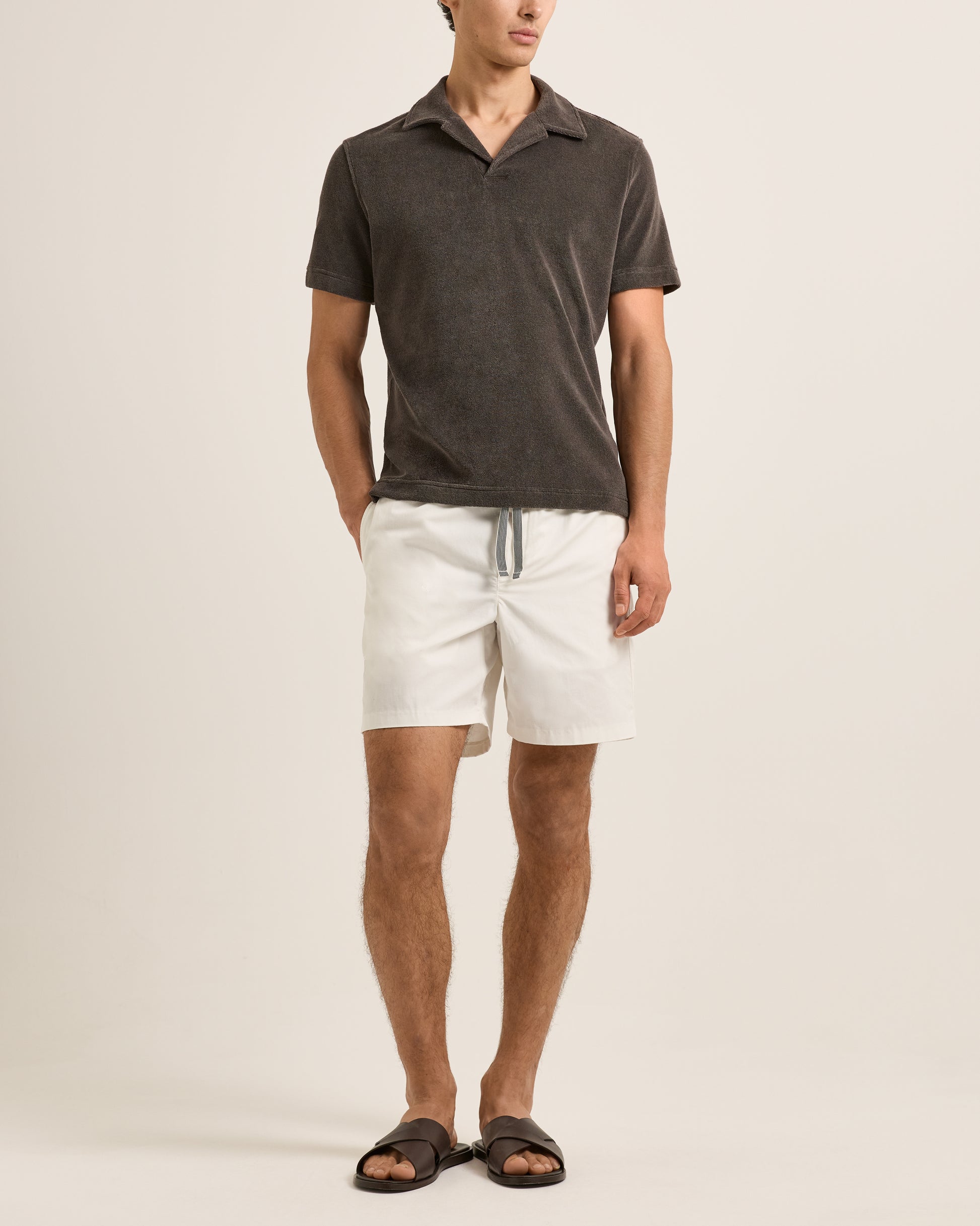 Man wearing a dark gray polo shirt and white shorts on a beige background