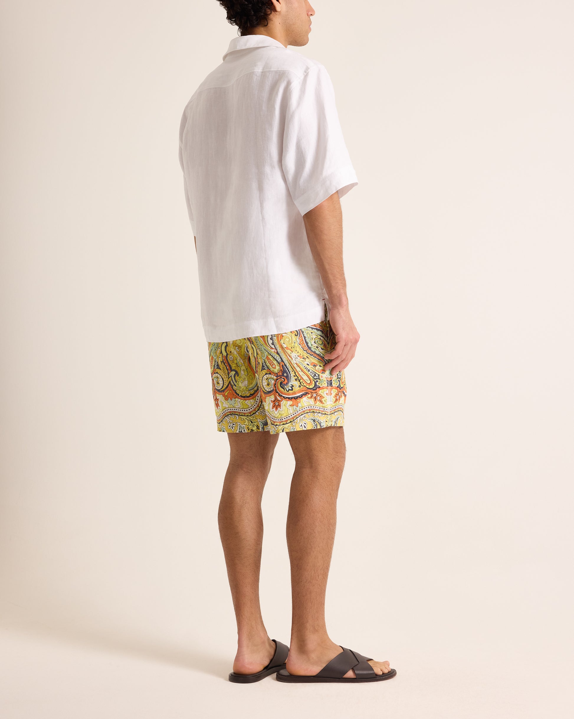 Person wearing a white polo shirt and colorful shorts on a beige background
