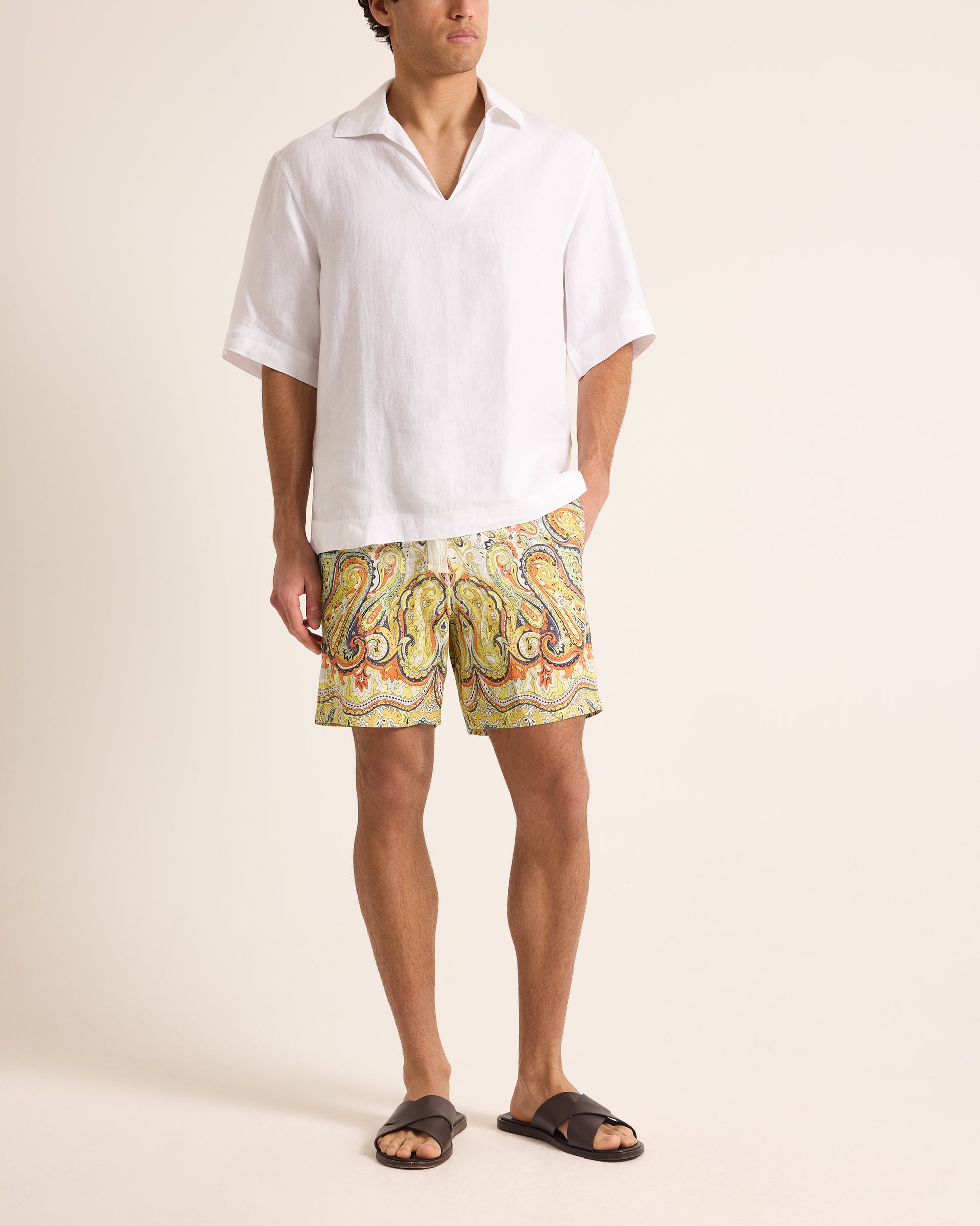 Man wearing a white shirt and colorful paisley shorts on a beige background