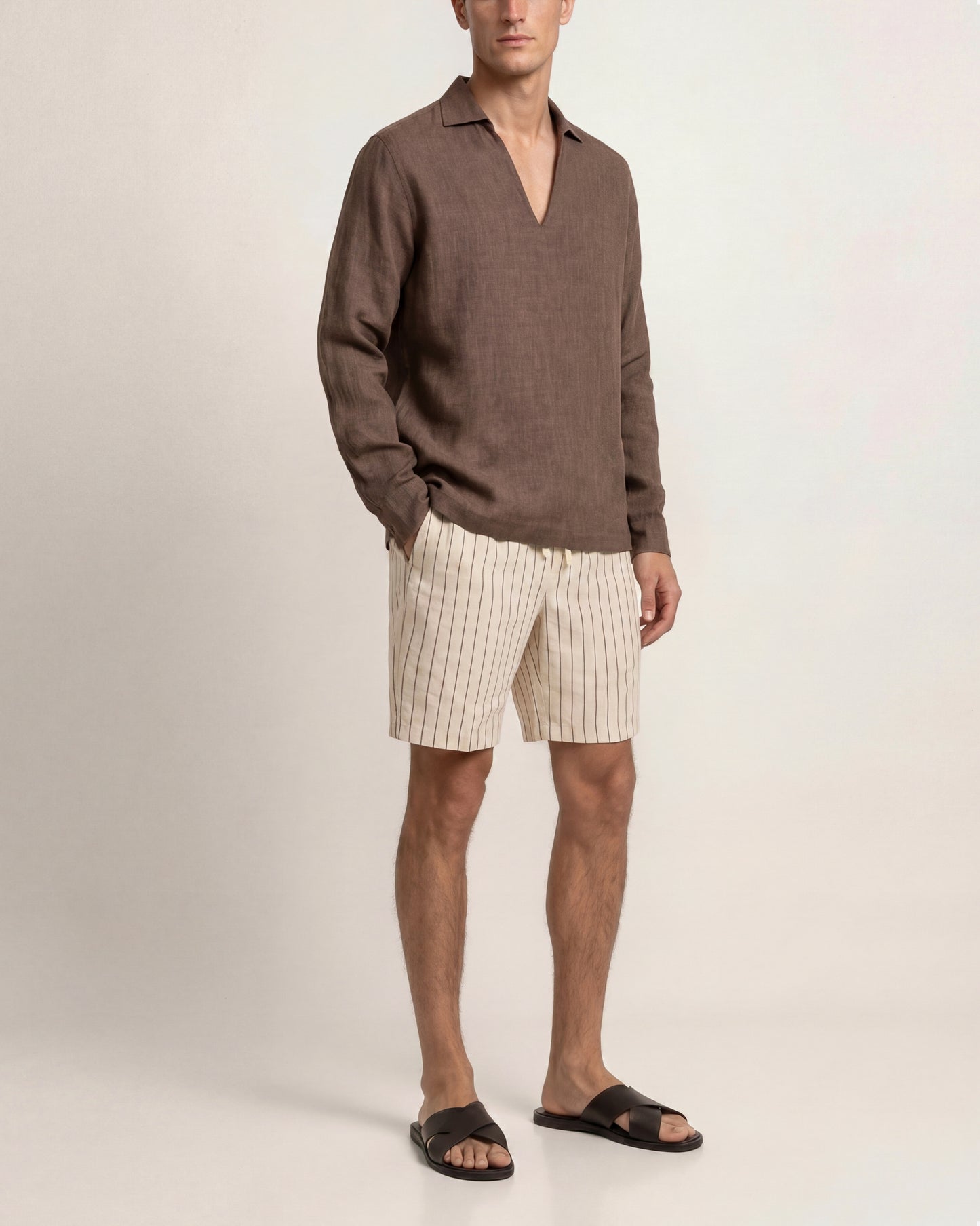 Man wearing a brown sweater and beige striped shorts on a plain background