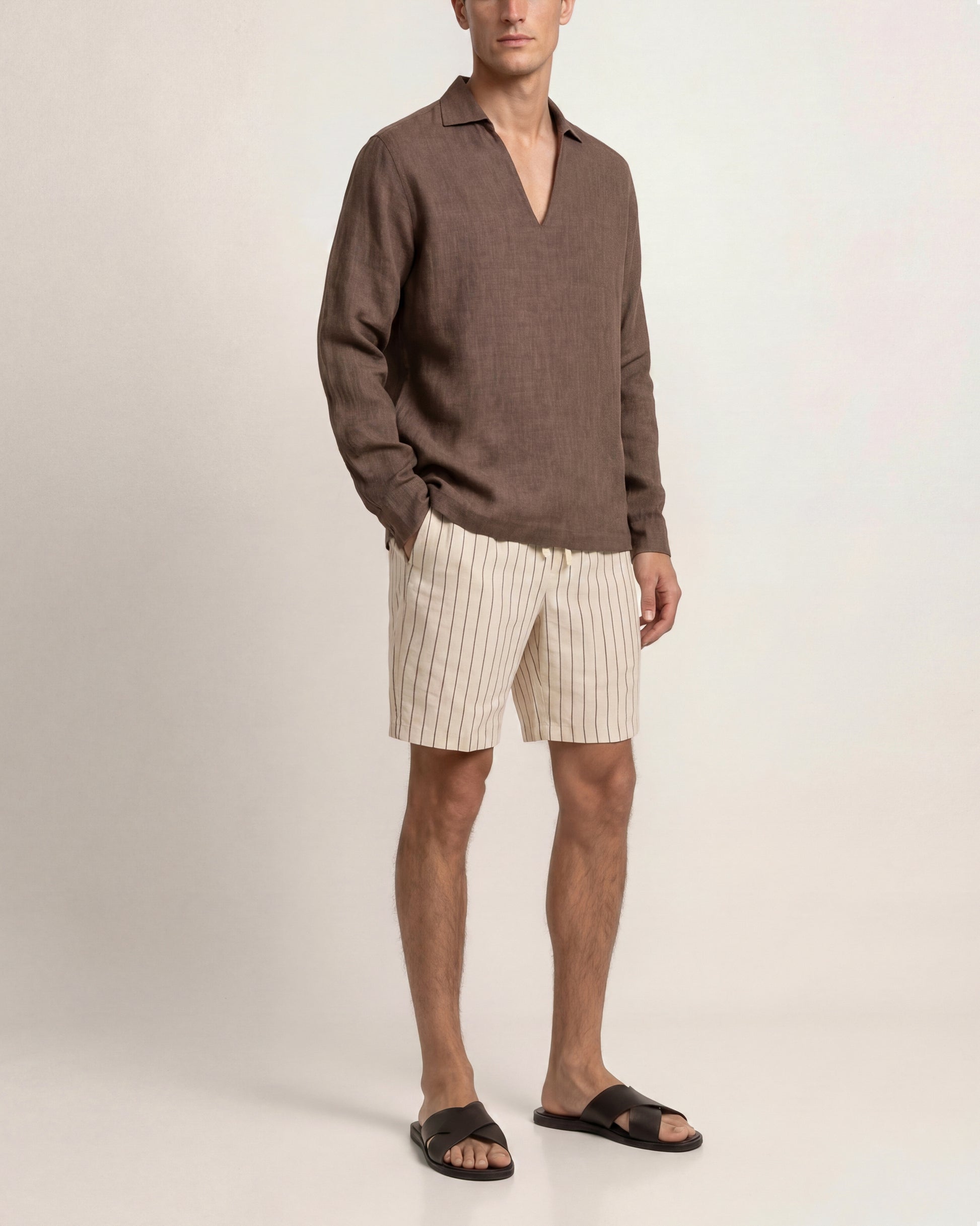 Man wearing a brown sweater and beige striped shorts on a plain background