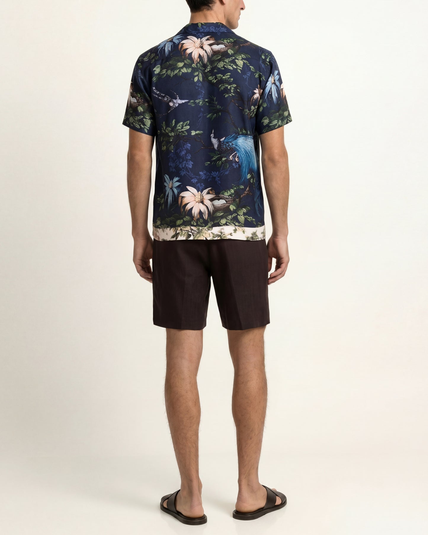 Man wearing a floral patterned shirt and black shorts on a white background