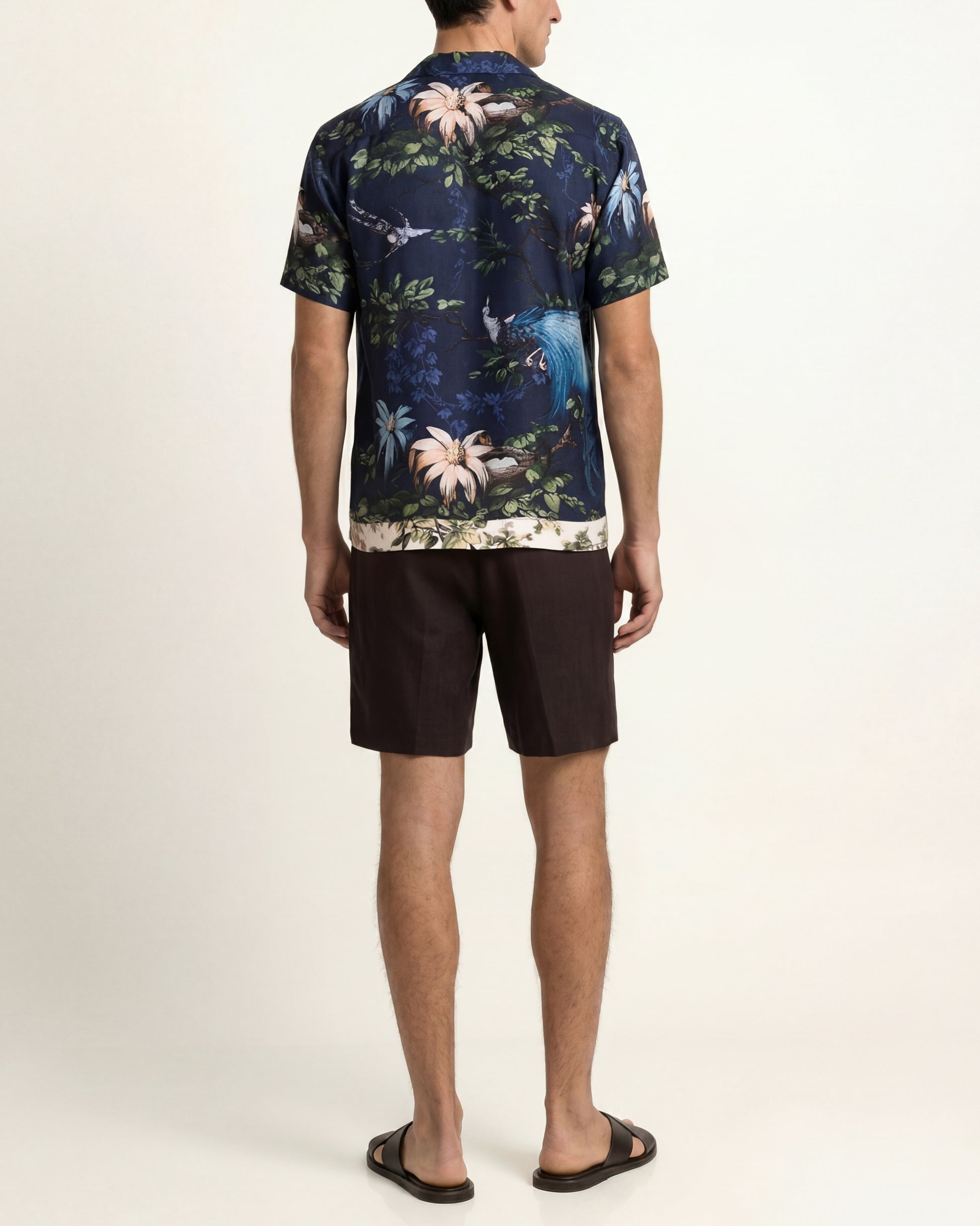 Man wearing a floral patterned shirt and black shorts on a white background