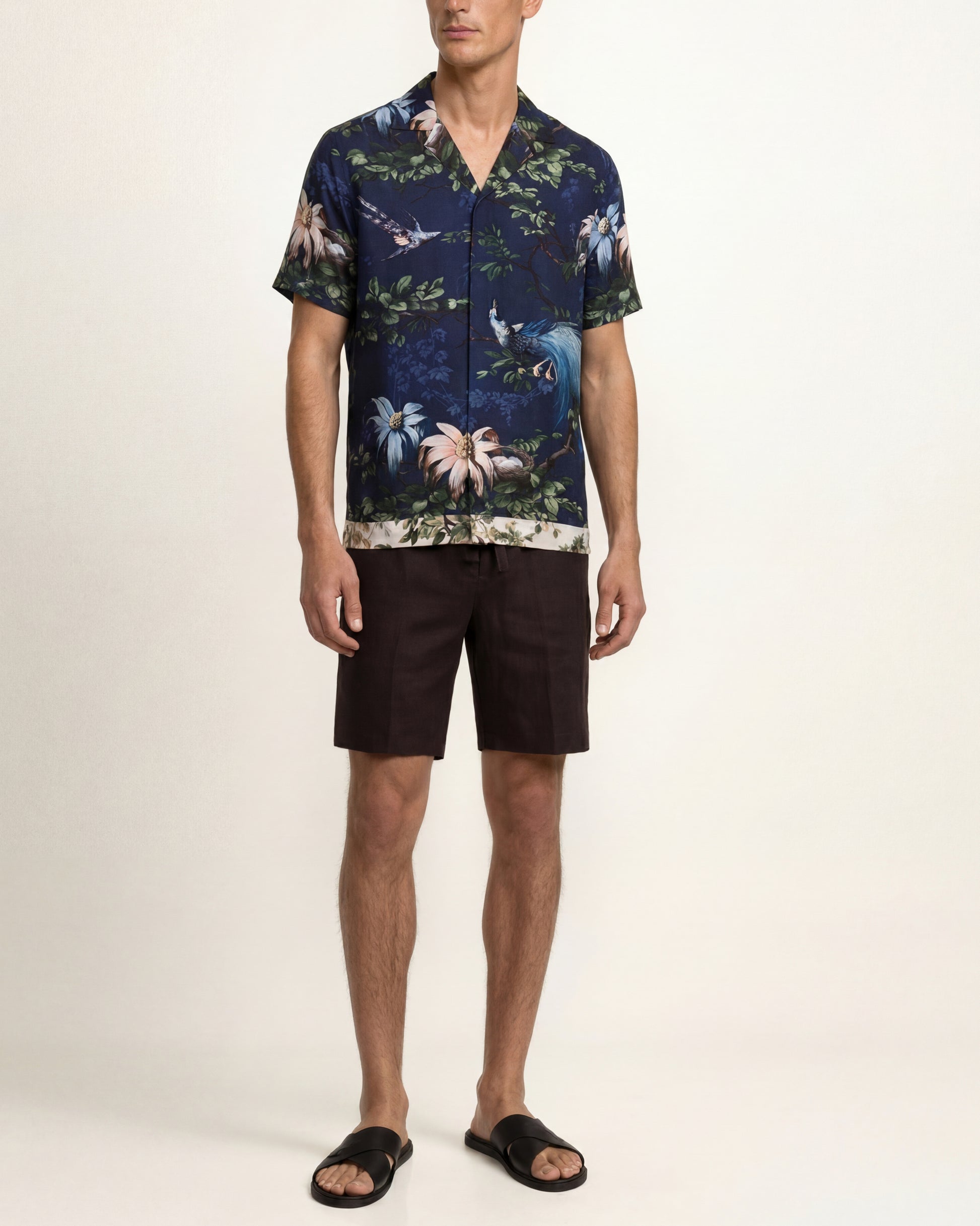 Man wearing a patterned shirt and shorts on a white background
