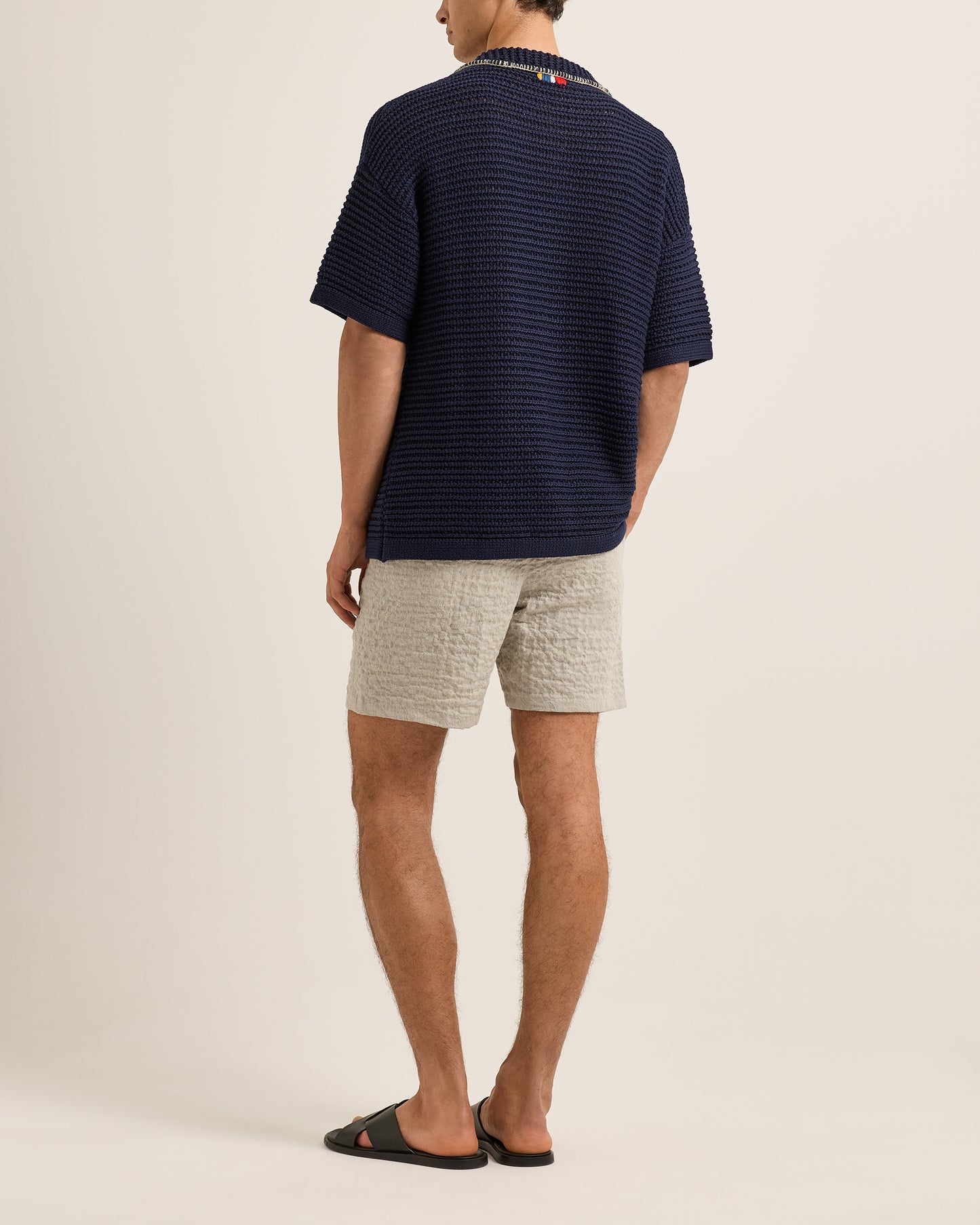 Man wearing a navy striped shirt and light gray shorts on a beige background