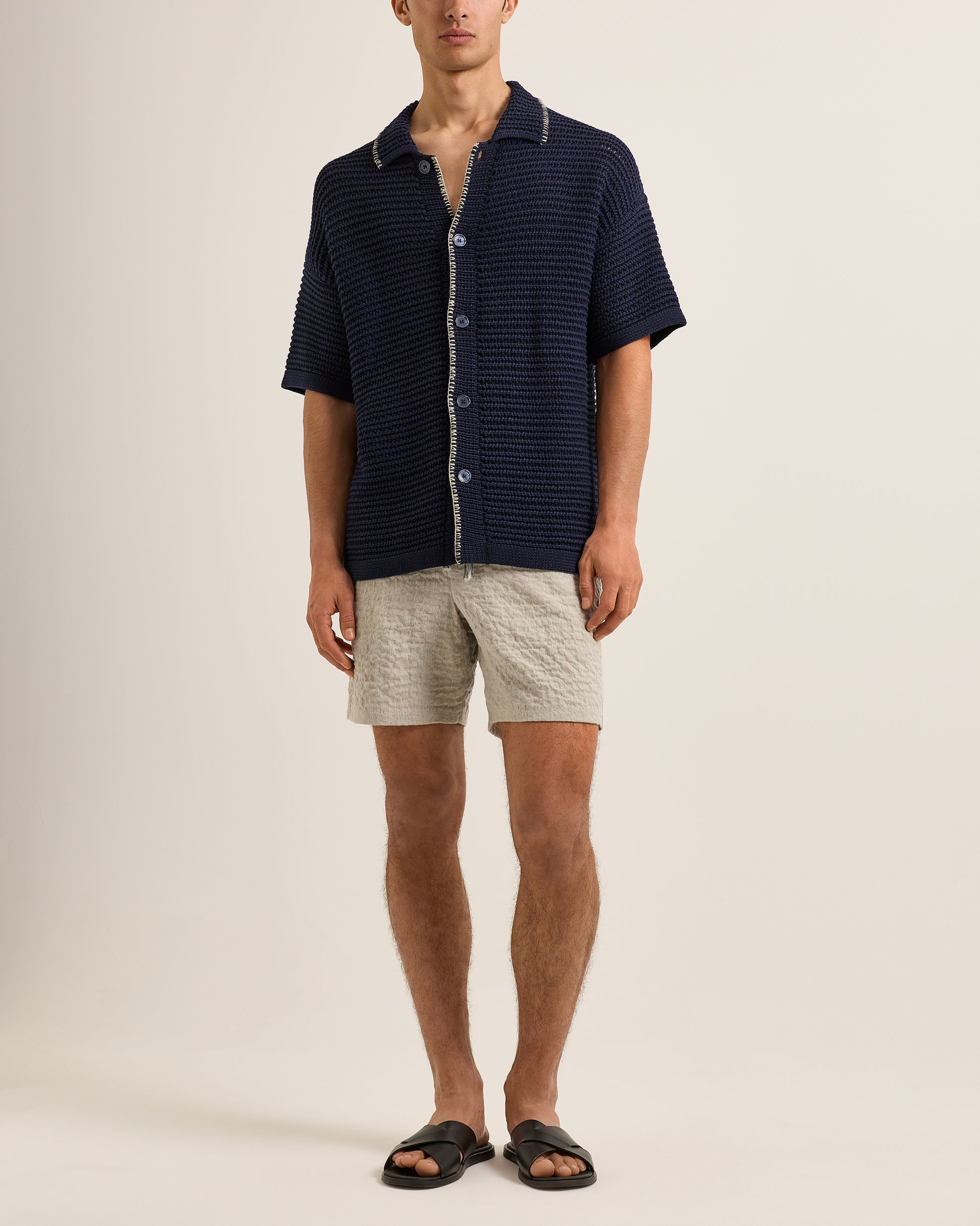 Man wearing a navy striped shirt and beige shorts on a plain background