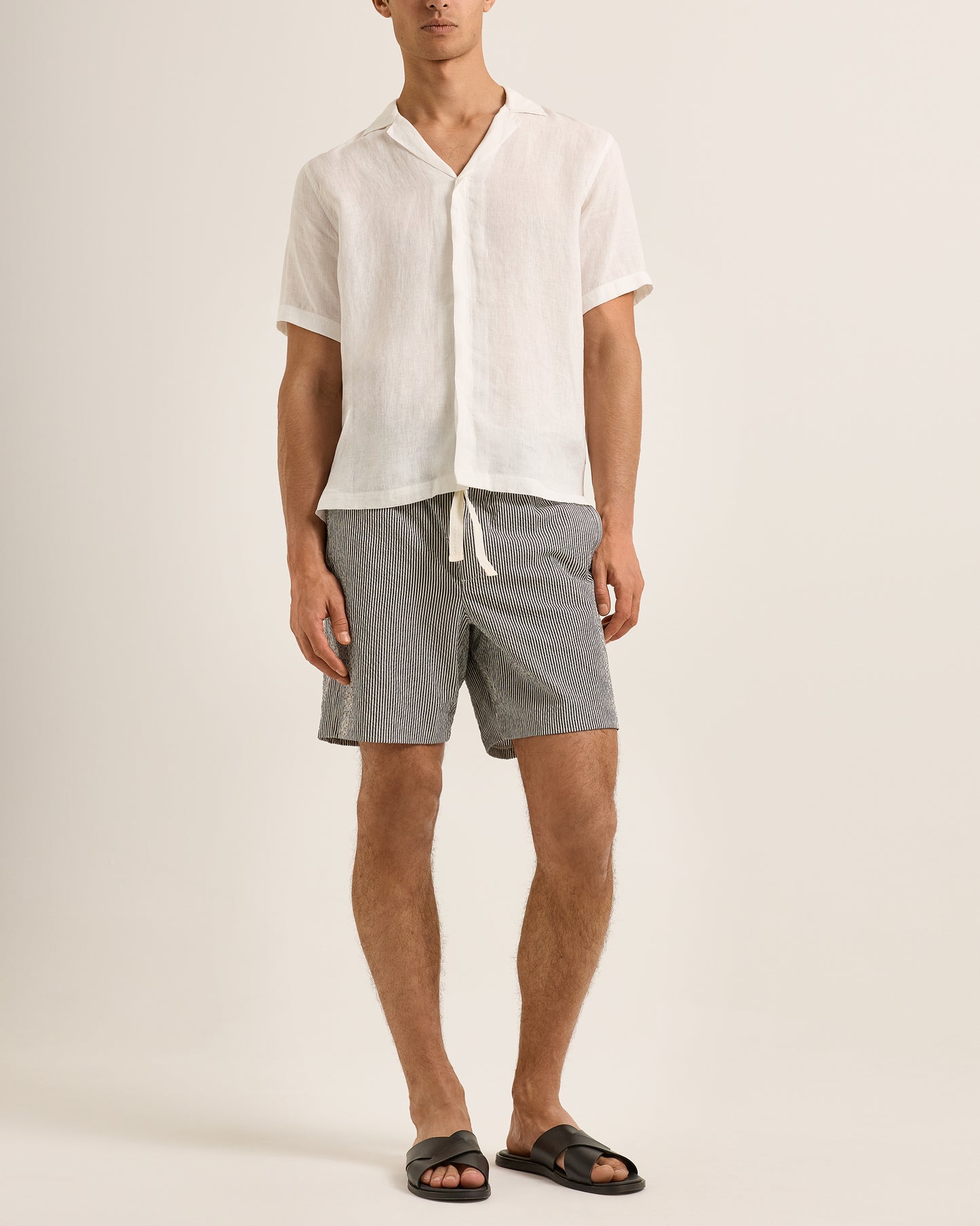 Person wearing a white shirt and gray shorts on a plain background