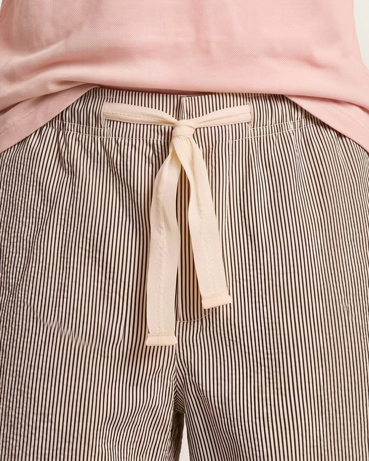 Close-up of white striped drawcord waist shorts paired with the hem of a light pink shirt