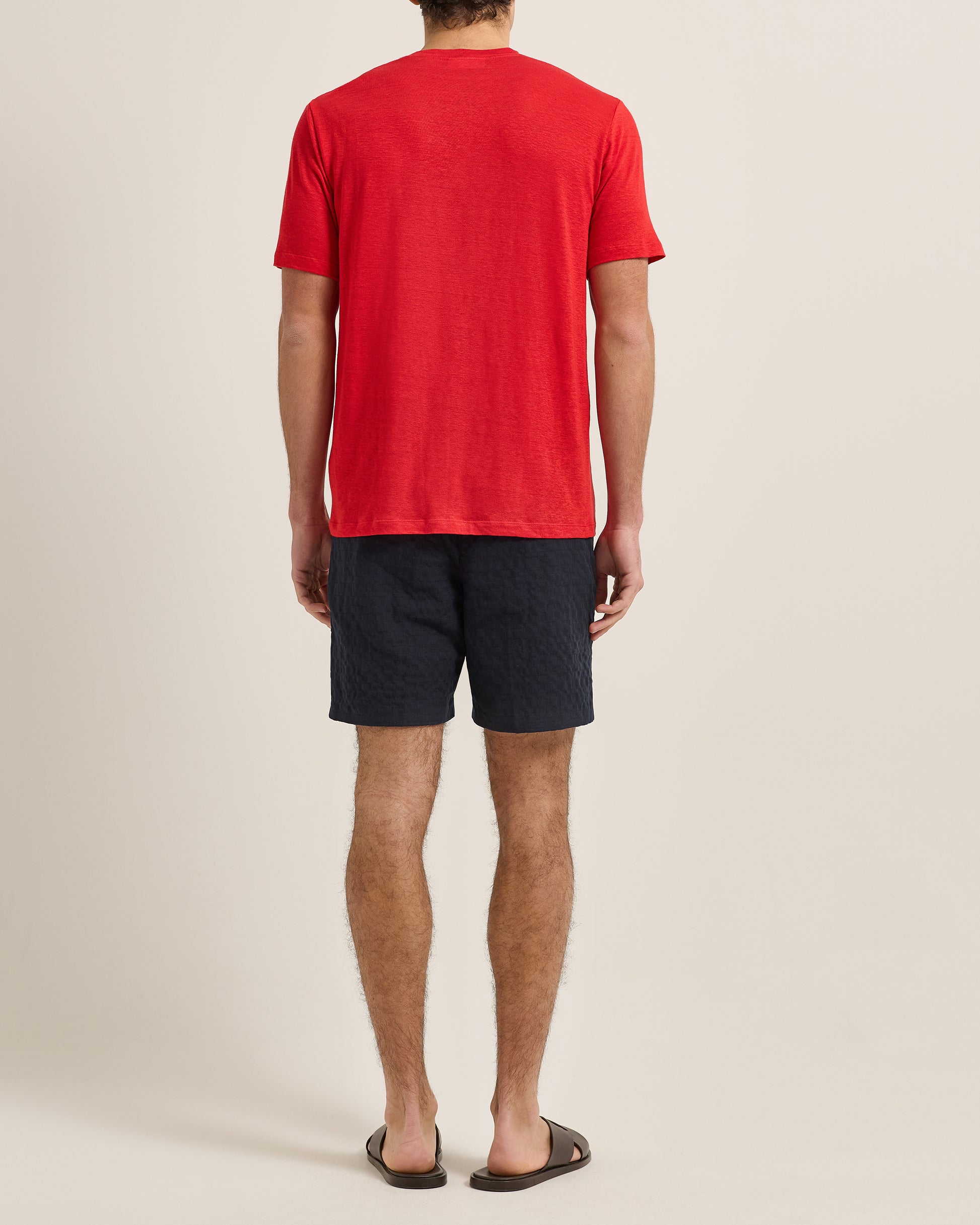 Person wearing a red t-shirt and dark shorts on a beige background