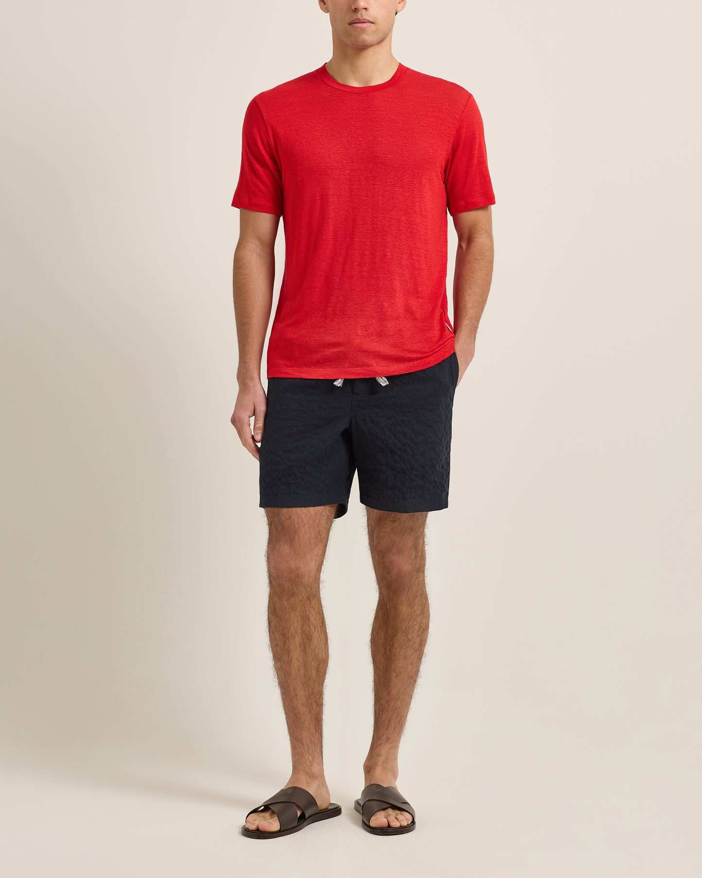 Person wearing a red t-shirt and dark shorts on a beige background