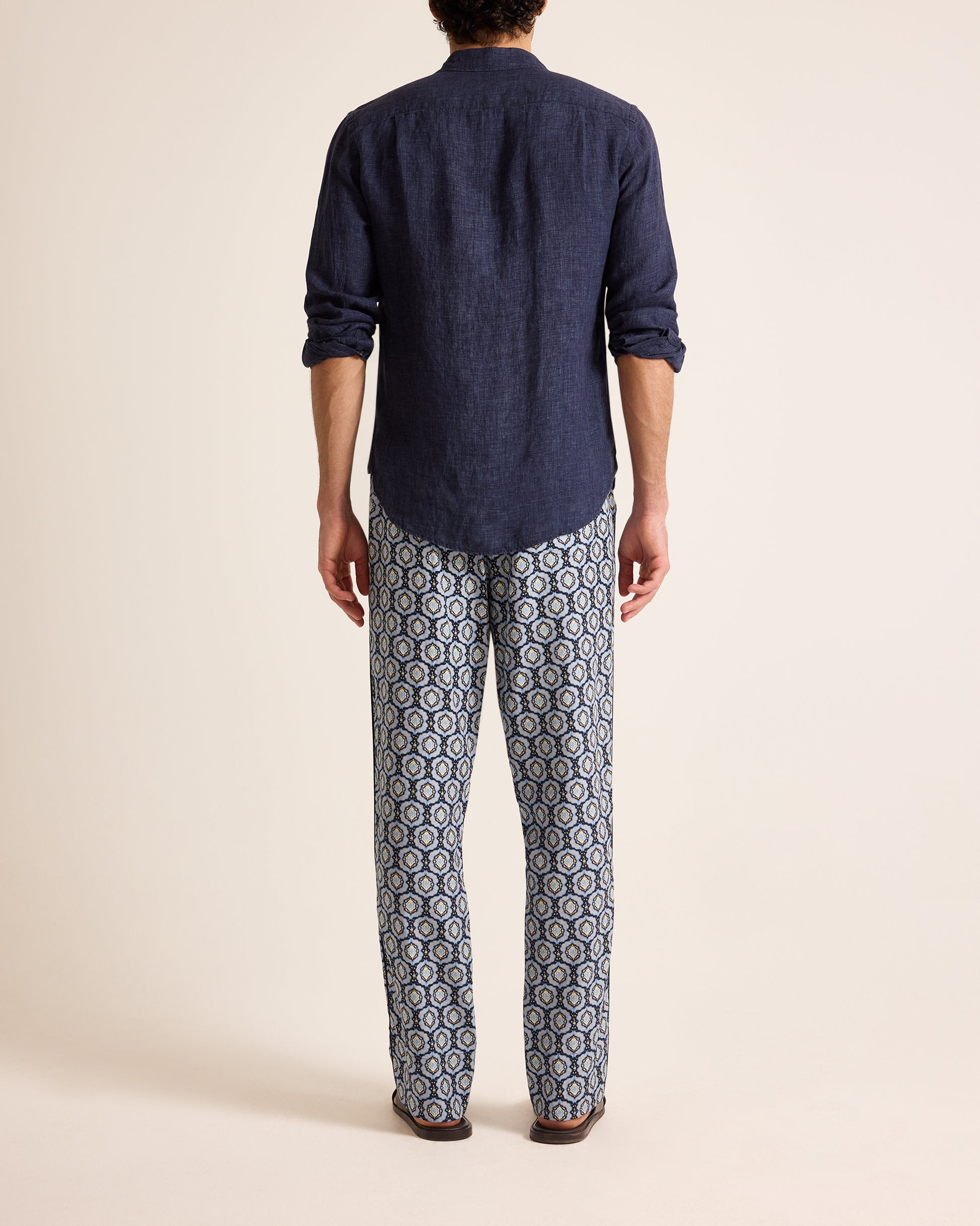 Person wearing a navy shirt and patterned pants on a beige background
