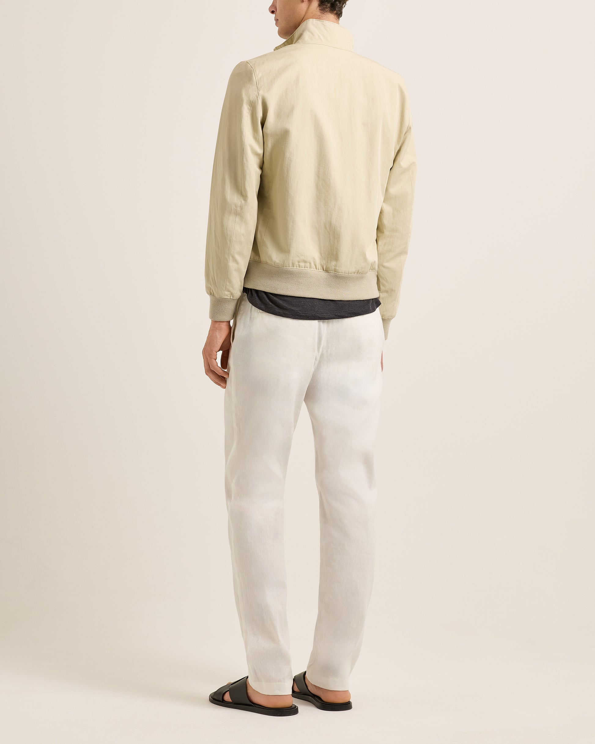 Person wearing a light-colored jacket and white pants on a plain background