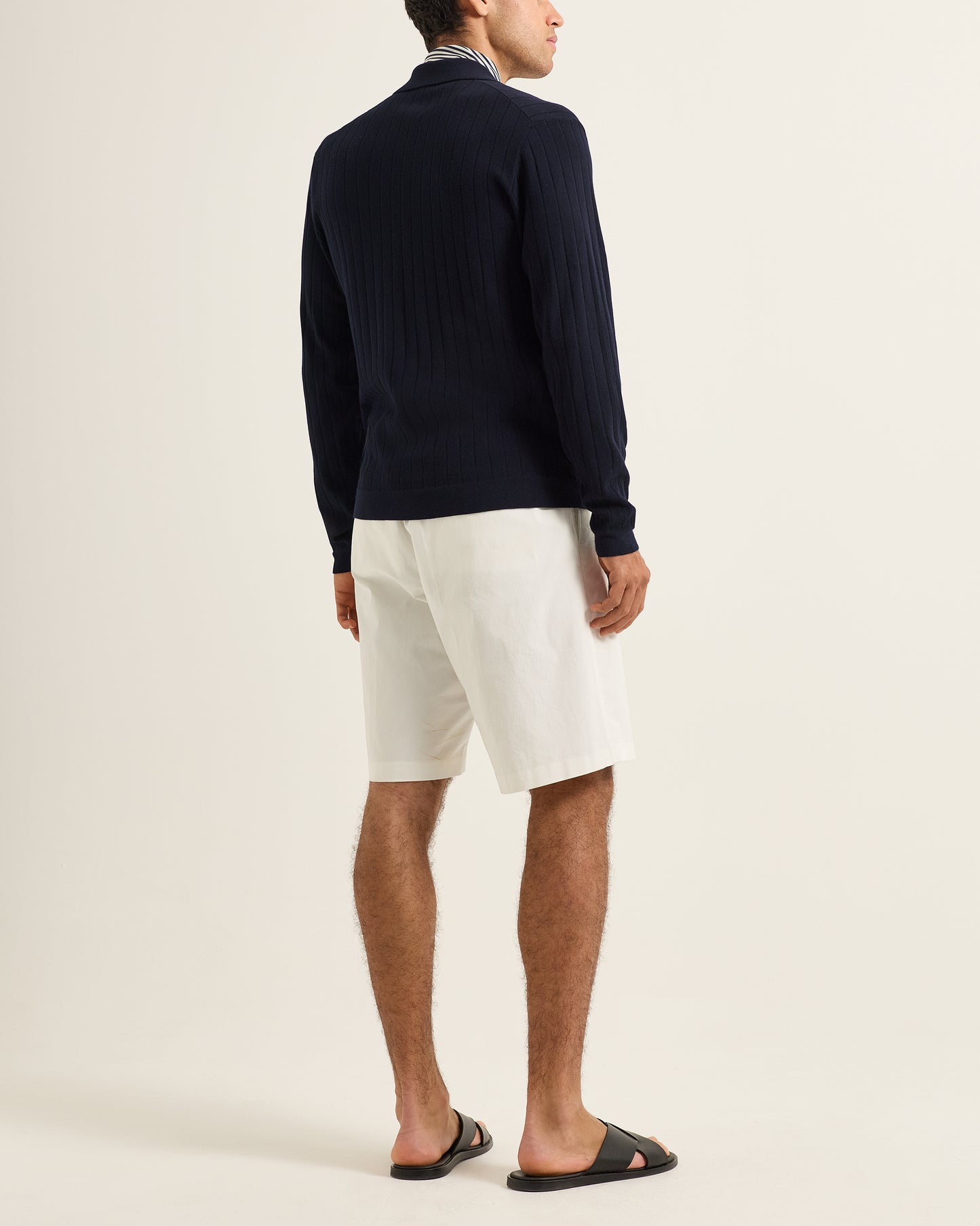 Person wearing a navy sweater and white shorts on a plain background