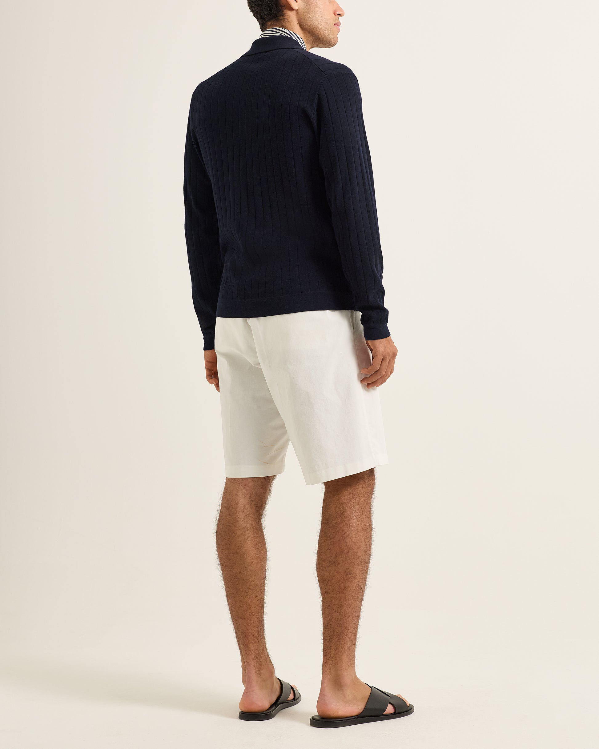 Person wearing a navy sweater and white shorts on a plain background