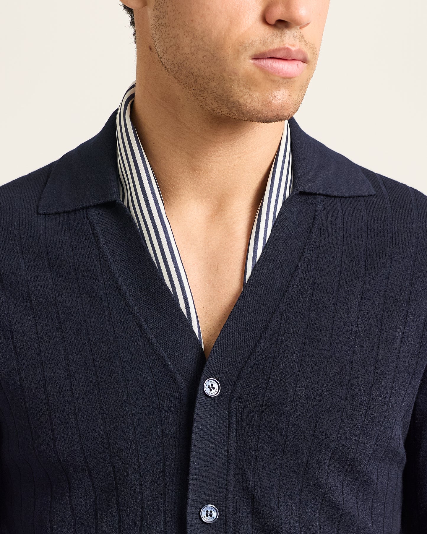 Navy cardigan over a striped shirt on a neutral background