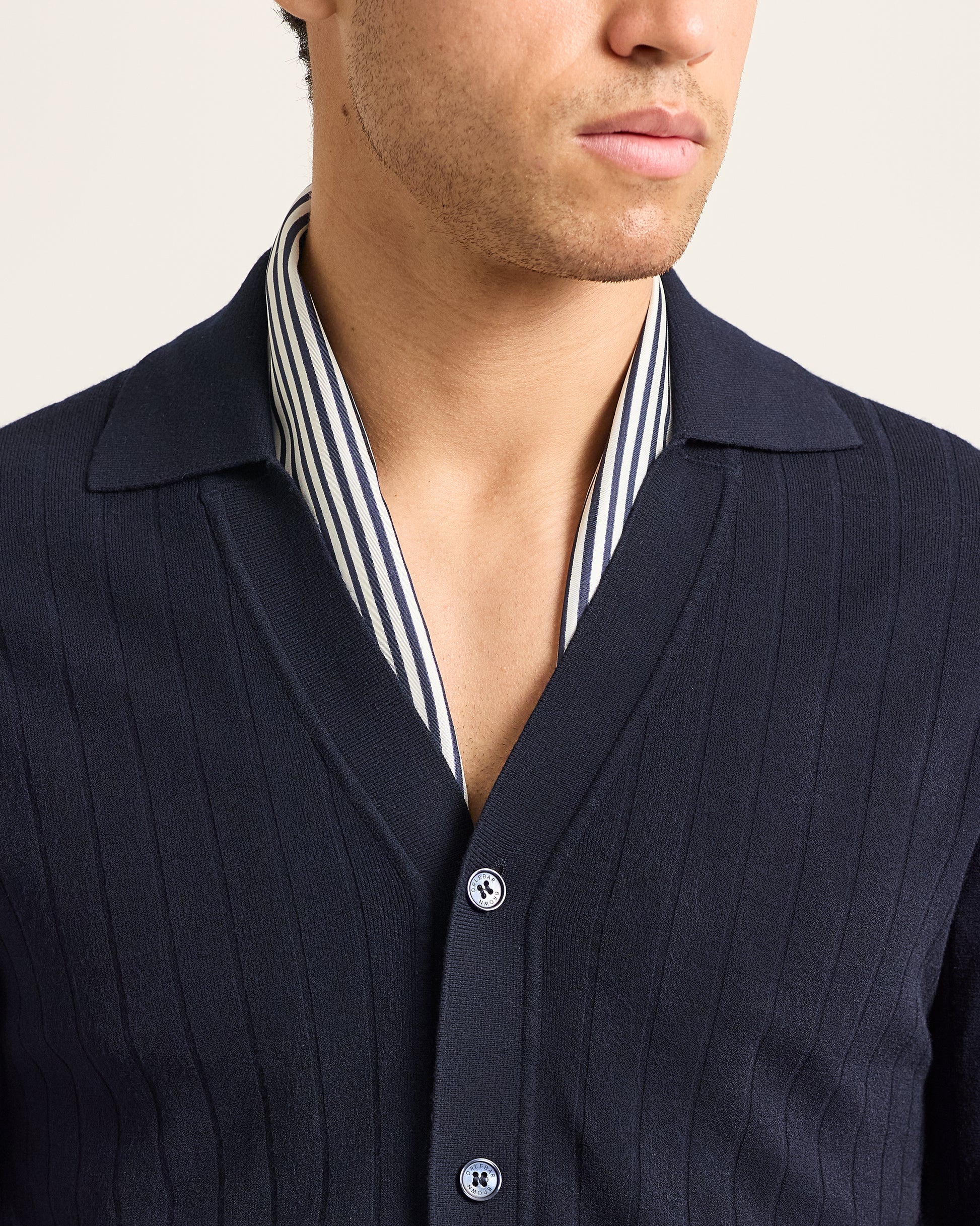 Navy cardigan over a striped shirt on a neutral background