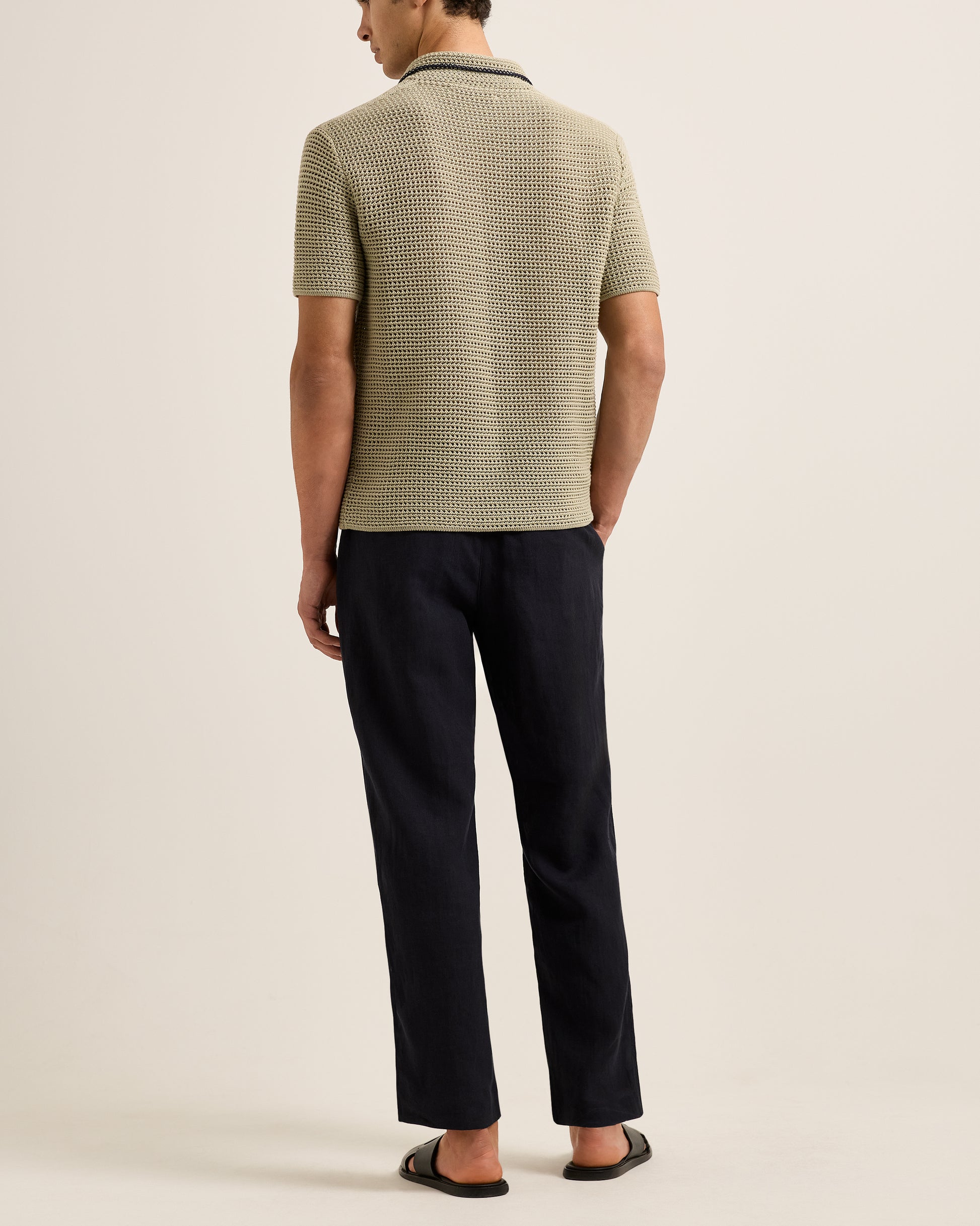 Man wearing a textured green polo shirt and black pants on a beige background