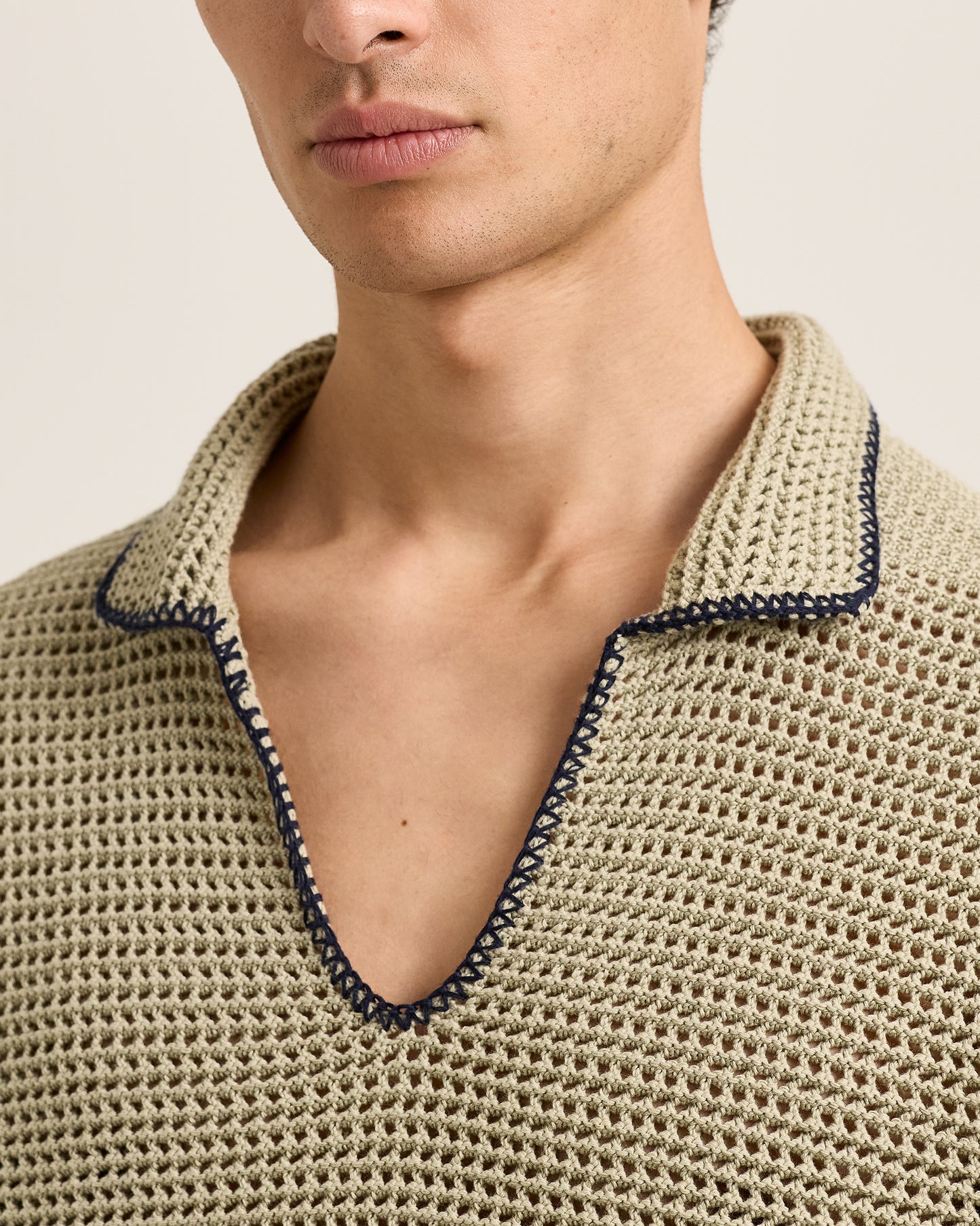 Close-up of a person wearing a beige knit shirt with a dark trim on a neutral background