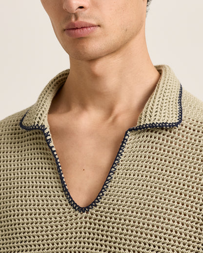 Close-up of a person wearing a beige knit shirt with a dark trim on a neutral background