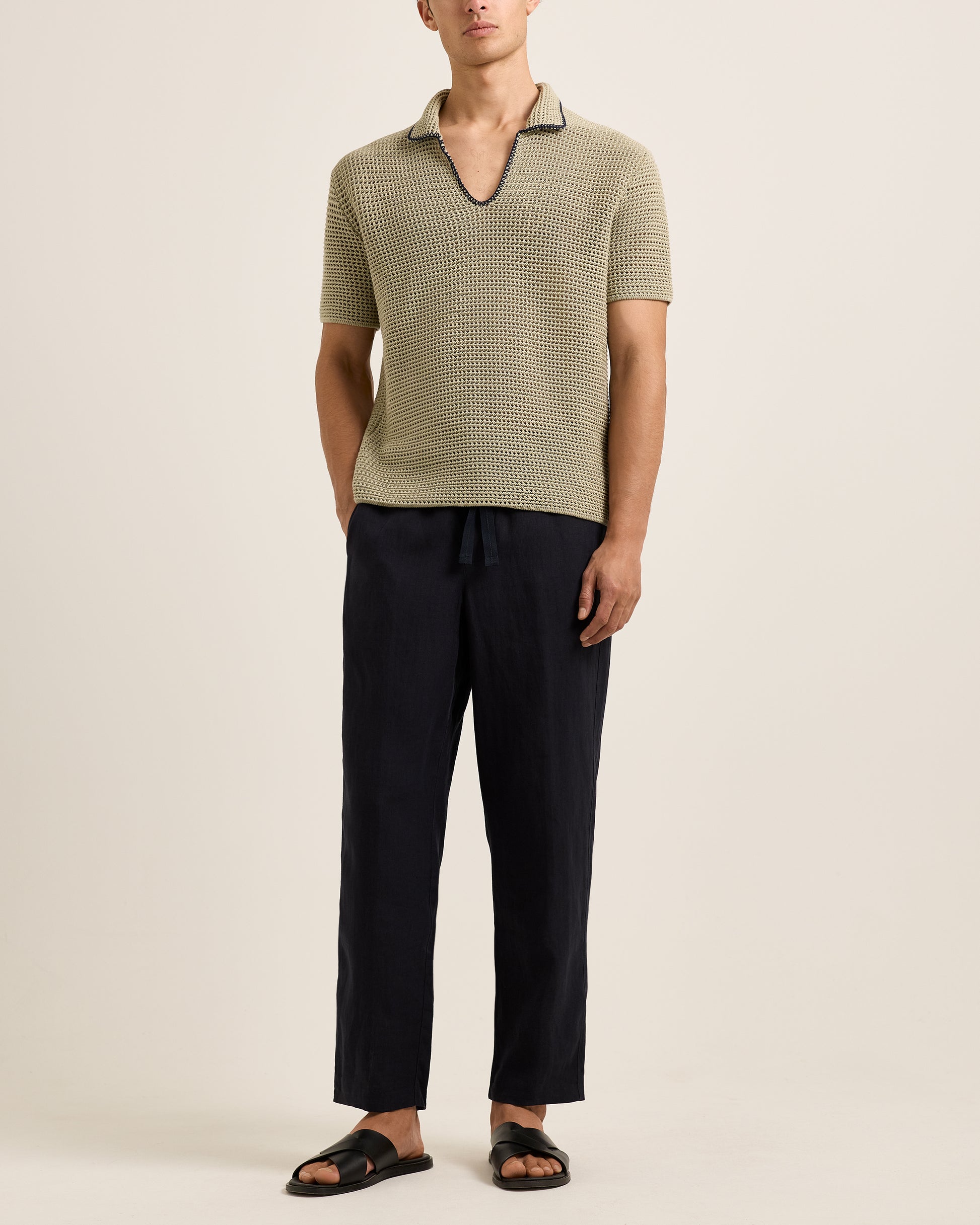 Man wearing a green textured polo shirt and black pants on a beige background