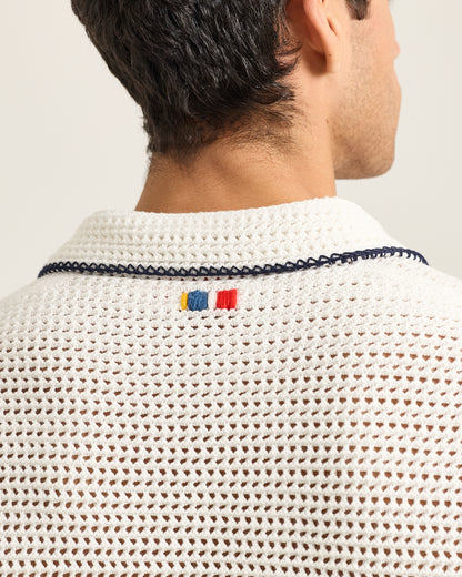 Close-up of a person wearing a textured white garment with a brand logo on a light background