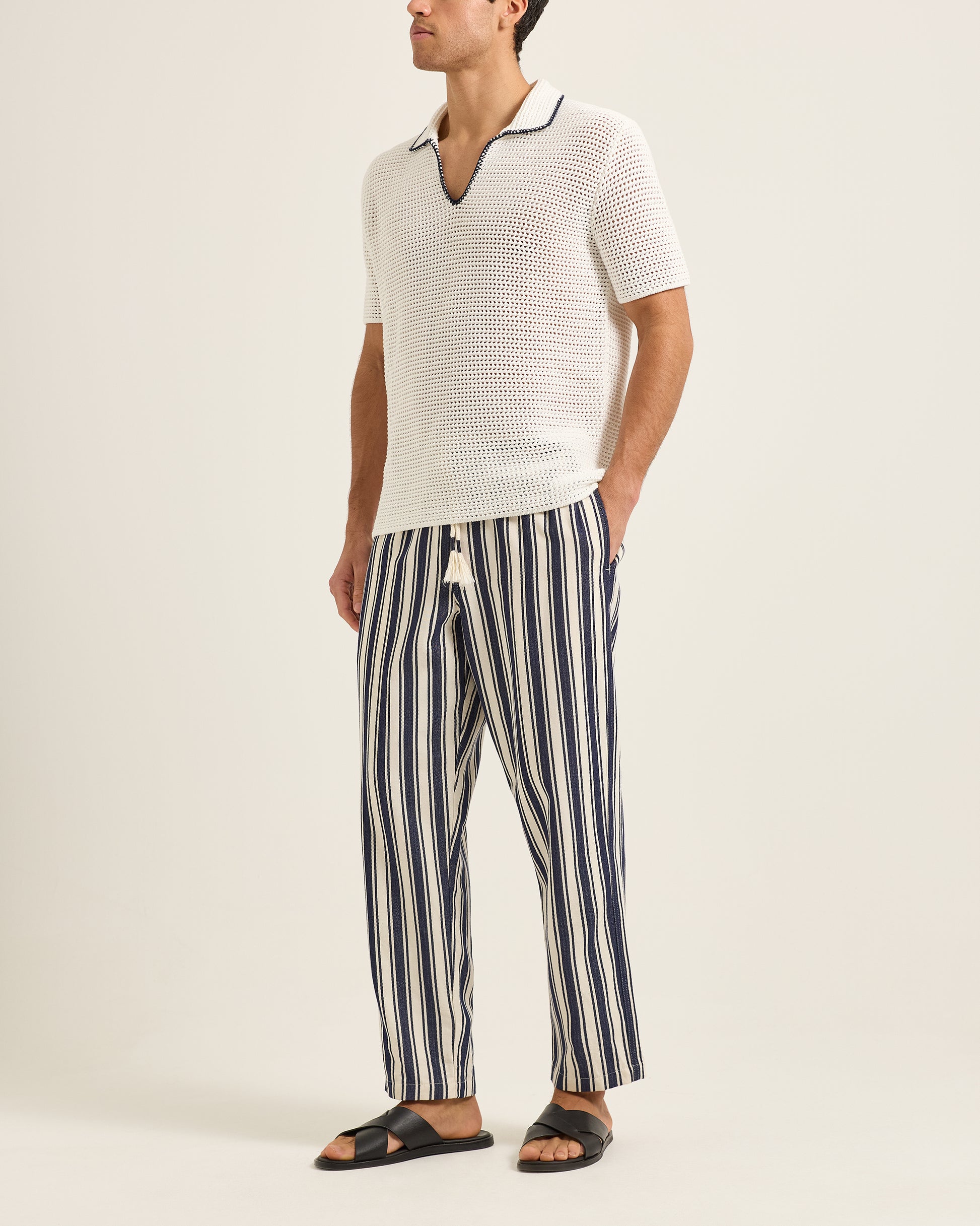 Man wearing a white textured polo shirt and striped pants on a plain background