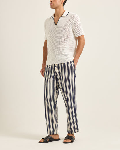 Man wearing a white textured polo shirt and striped pants on a plain background