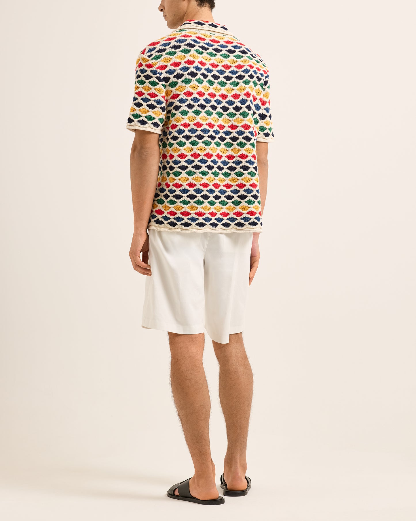 Person wearing a colorful geometric patterned polo shirt and white shorts on a beige background