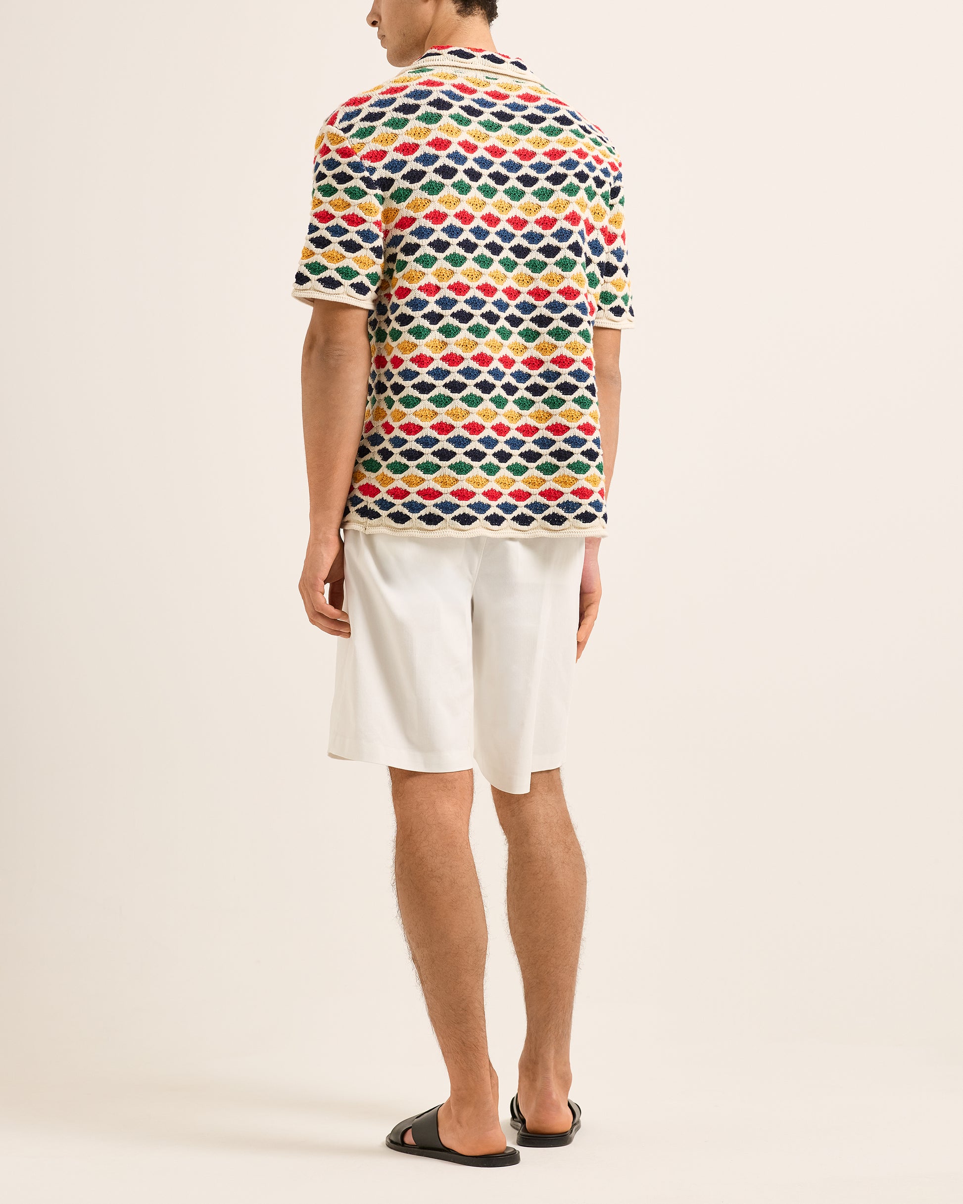 Person wearing a colorful geometric patterned polo shirt and white shorts on a beige background