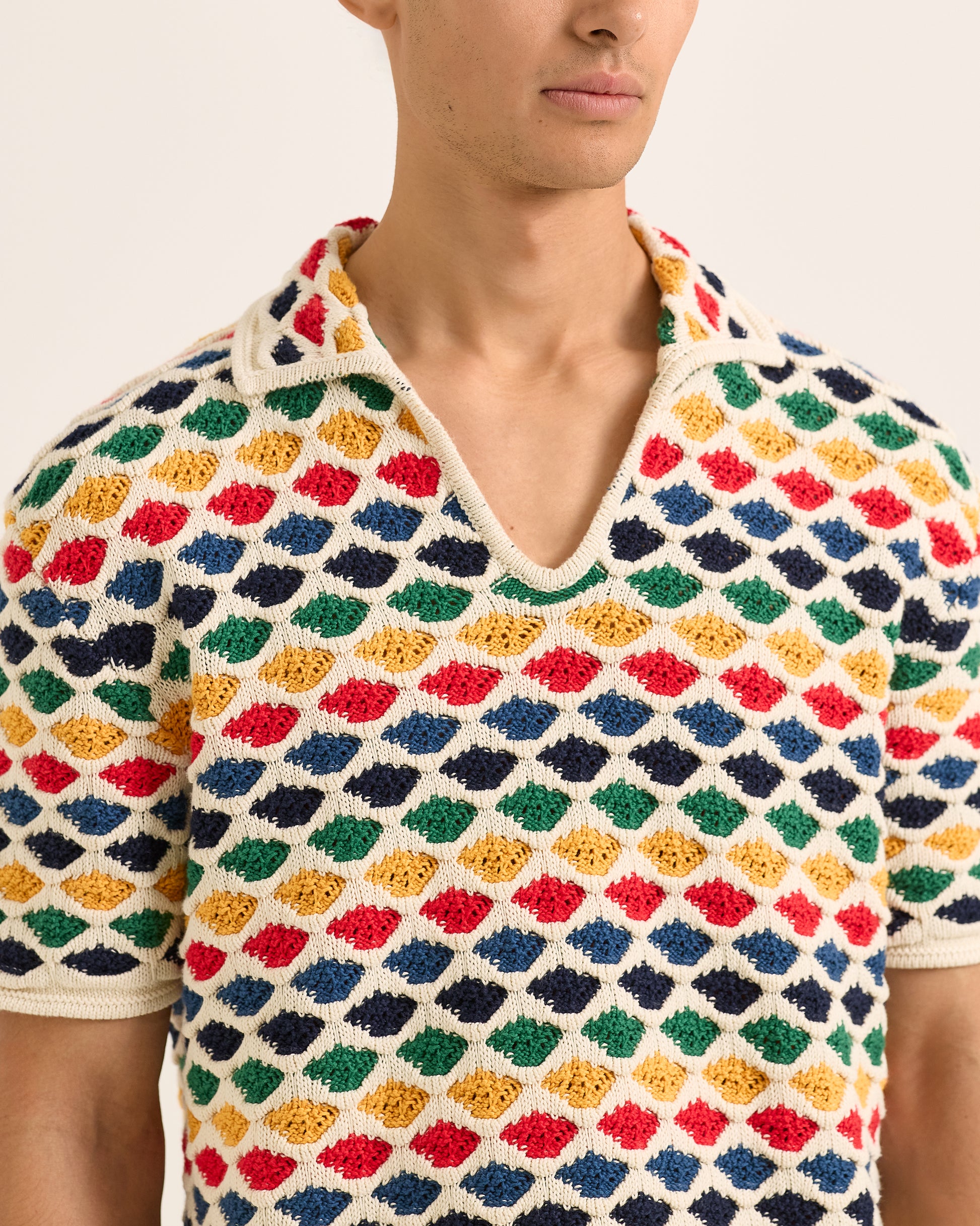 Person wearing a colorful diamond patterned shirt with a neutral background