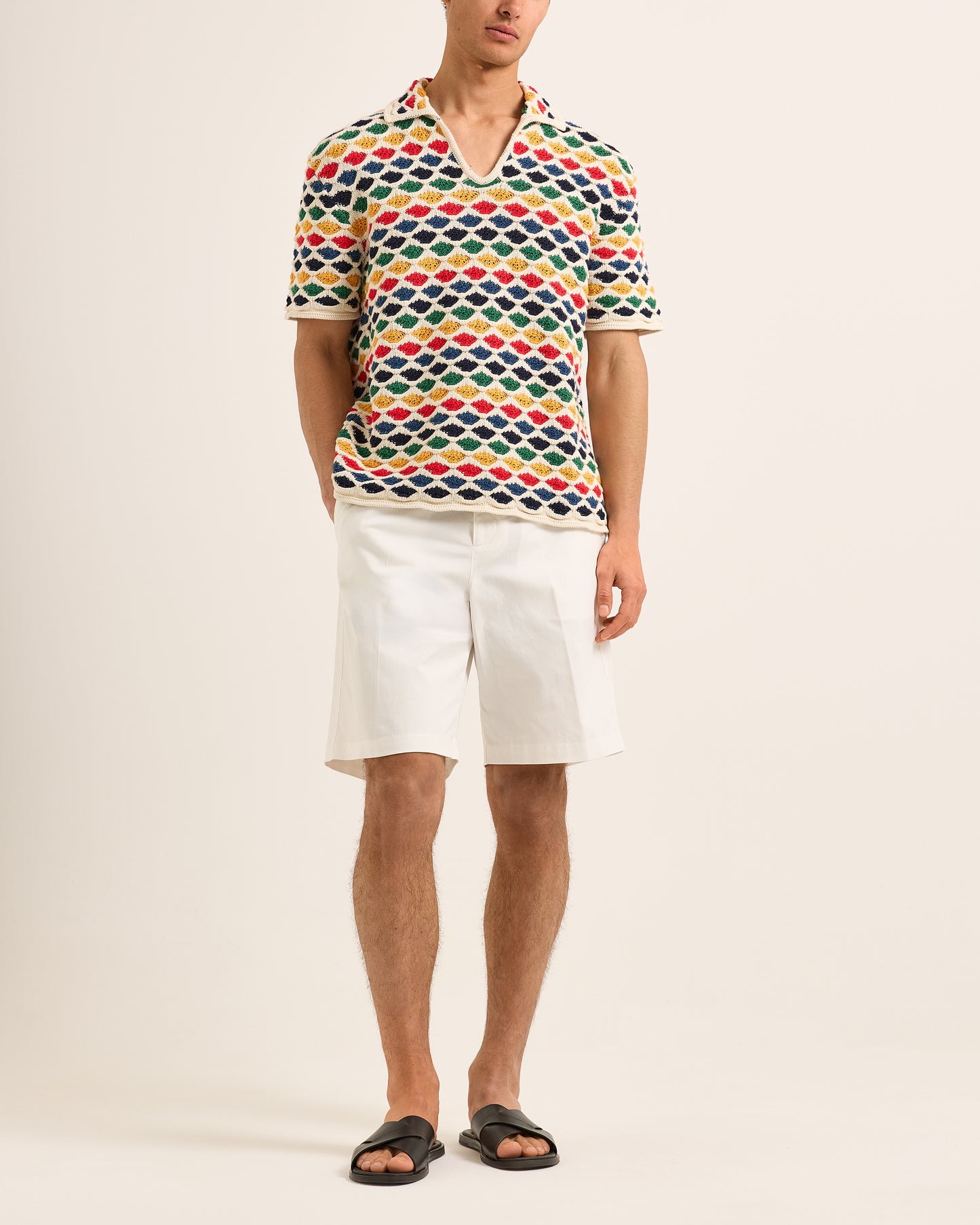 Person wearing a colorful geometric patterned polo shirt and white shorts on a beige background