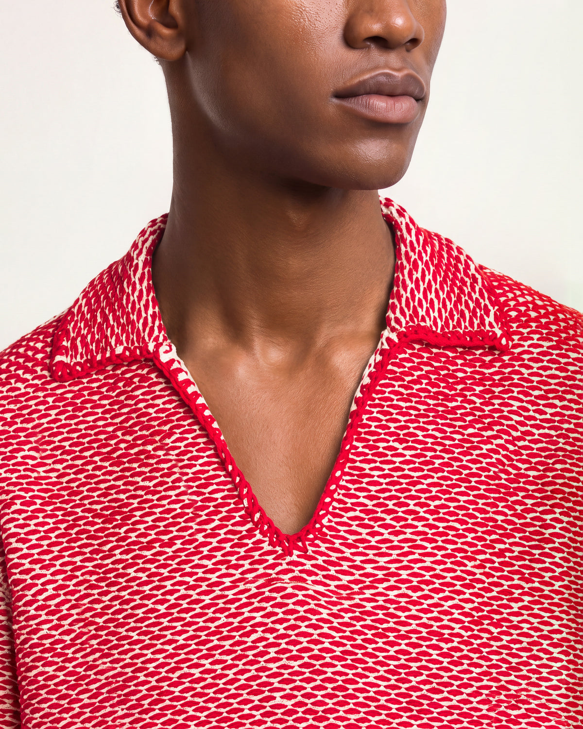 Close-up of a man wearing a red-and-white crochet knit polo shirt on a plain background