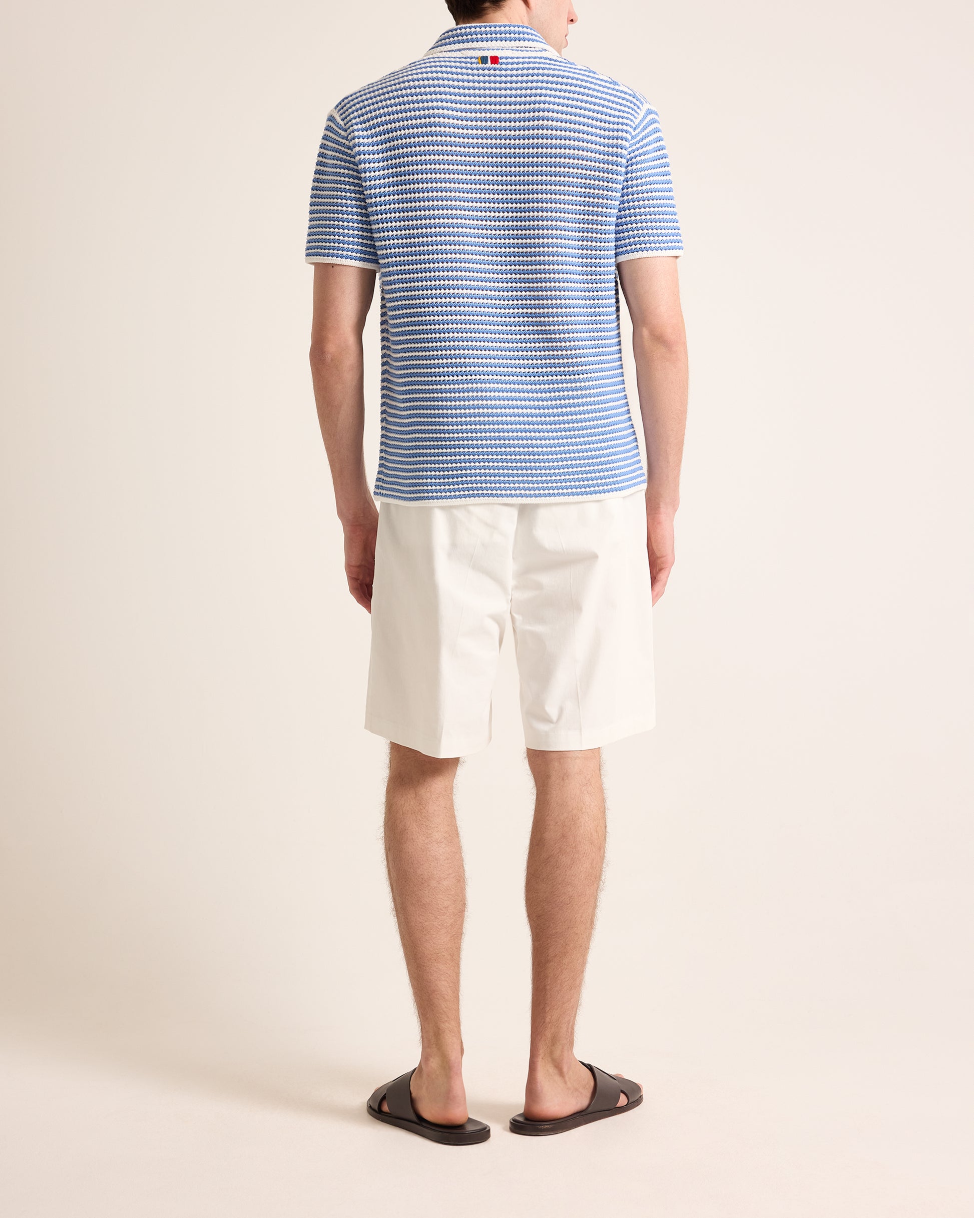 Person wearing a blue striped polo shirt and white shorts on a beige background