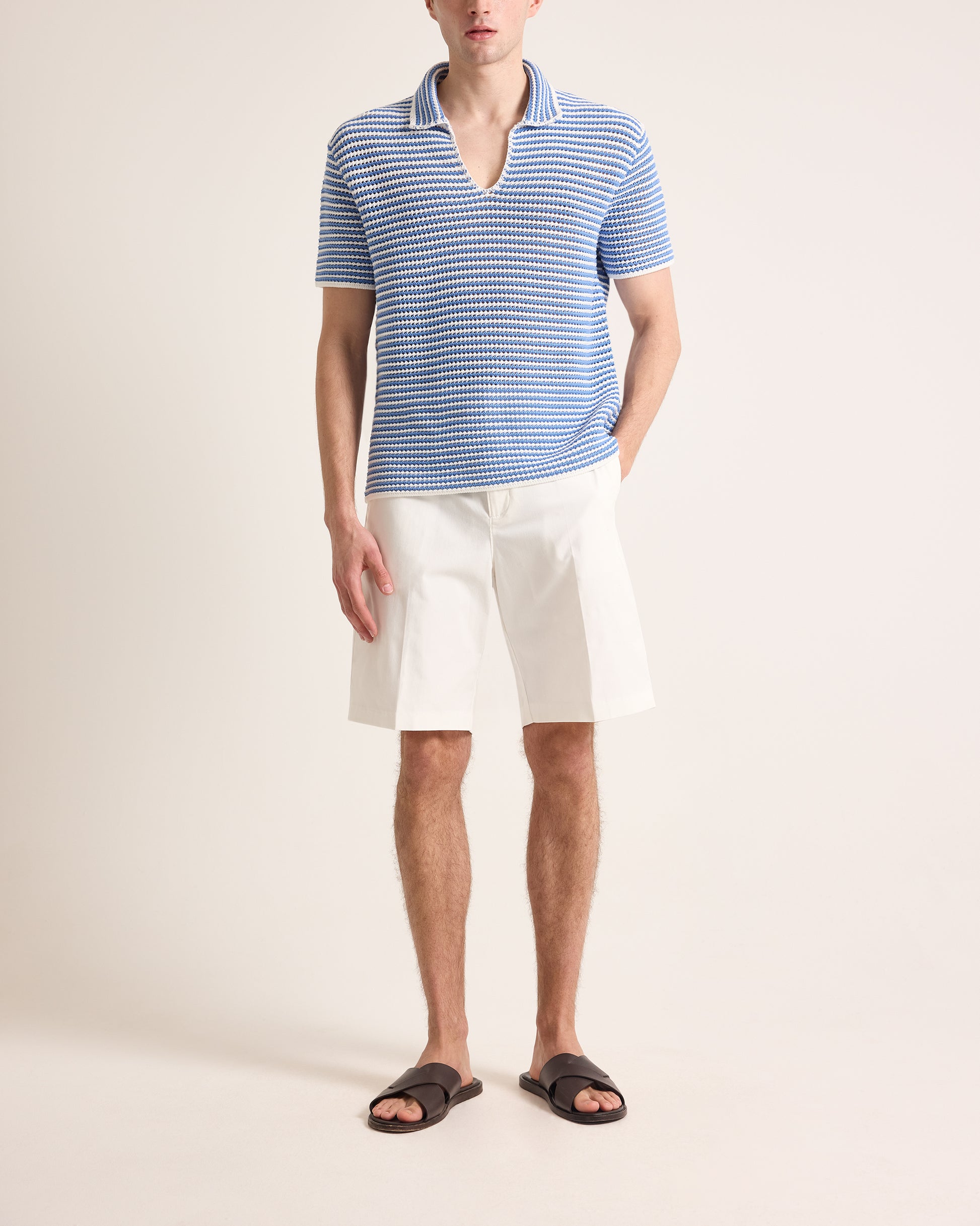 Man wearing a blue striped polo shirt and white shorts on a plain background