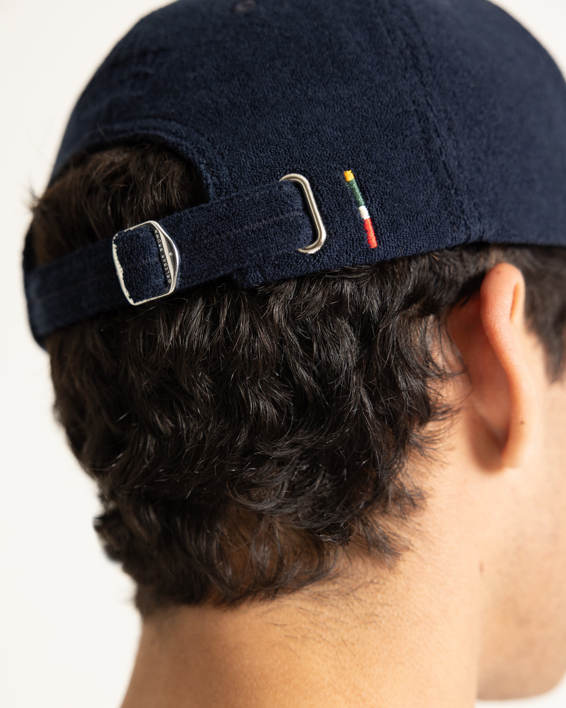 Close-up back view of a person wearing a dark navy blue baseball cap with an adjustable strap and silver metal buckle.