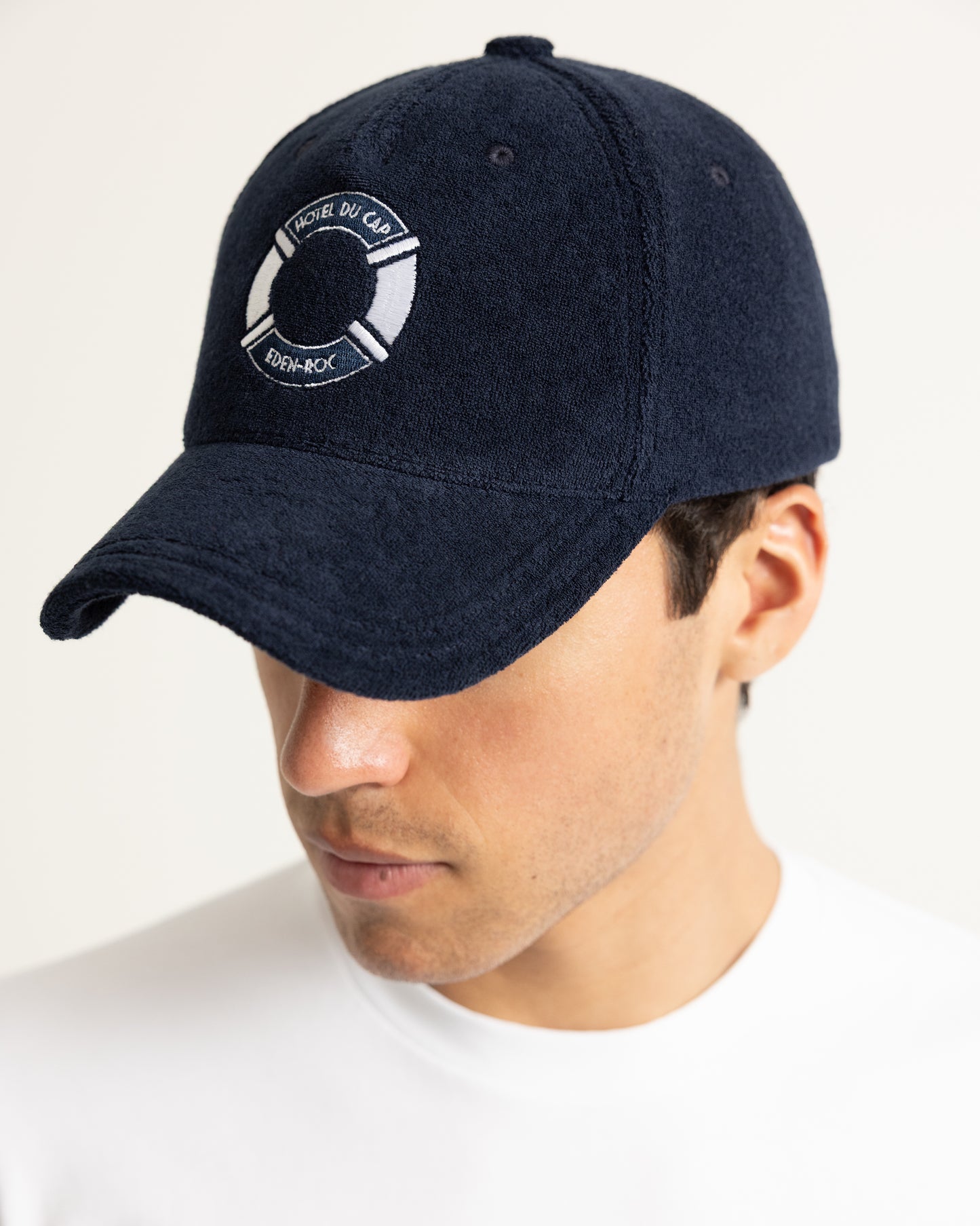 A man wearing a dark navy blue textured baseball cap with a white circular logo on the front 