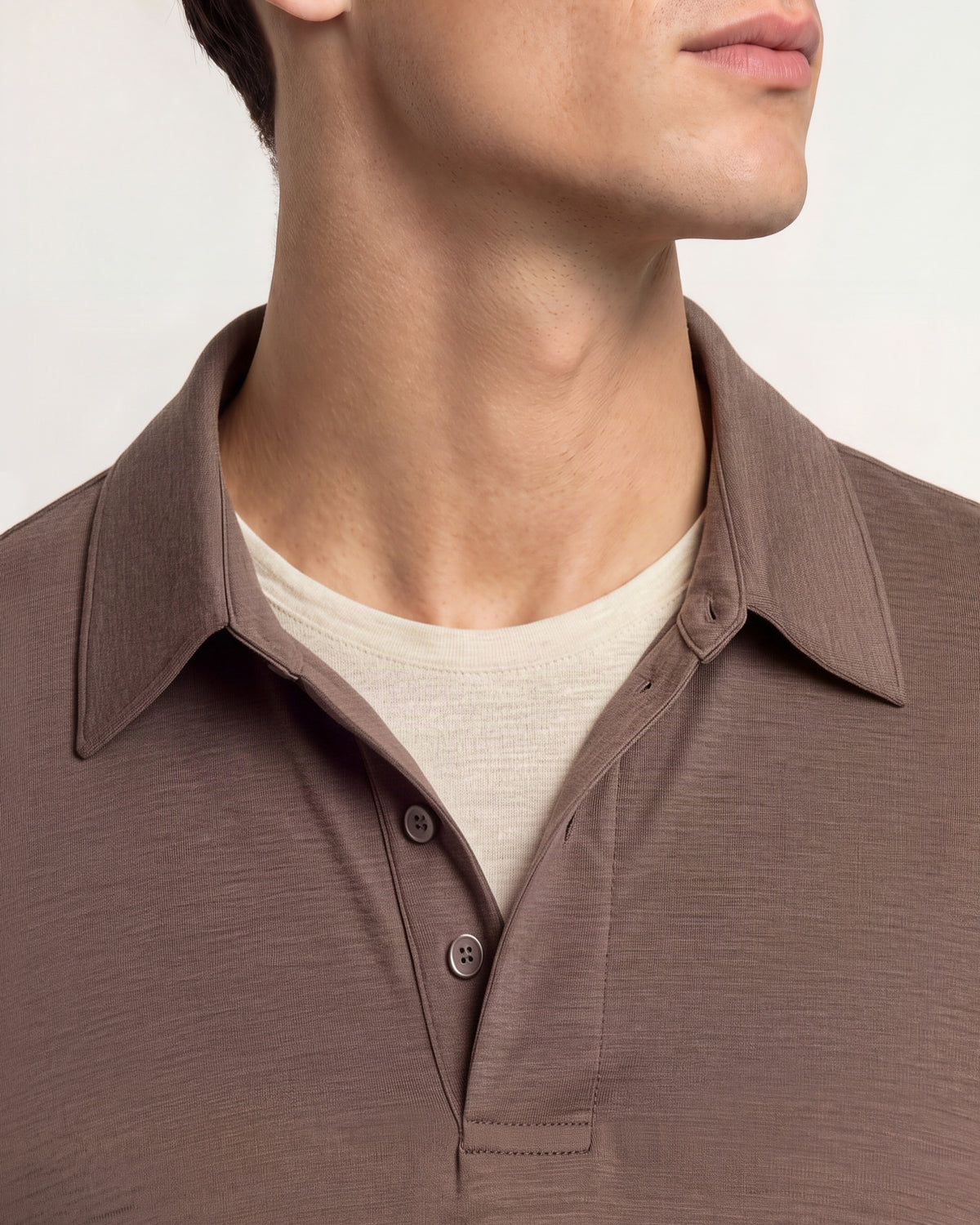 Closeup of man wearing brown polo shirt with beige t-shirt underneath on a plain background
