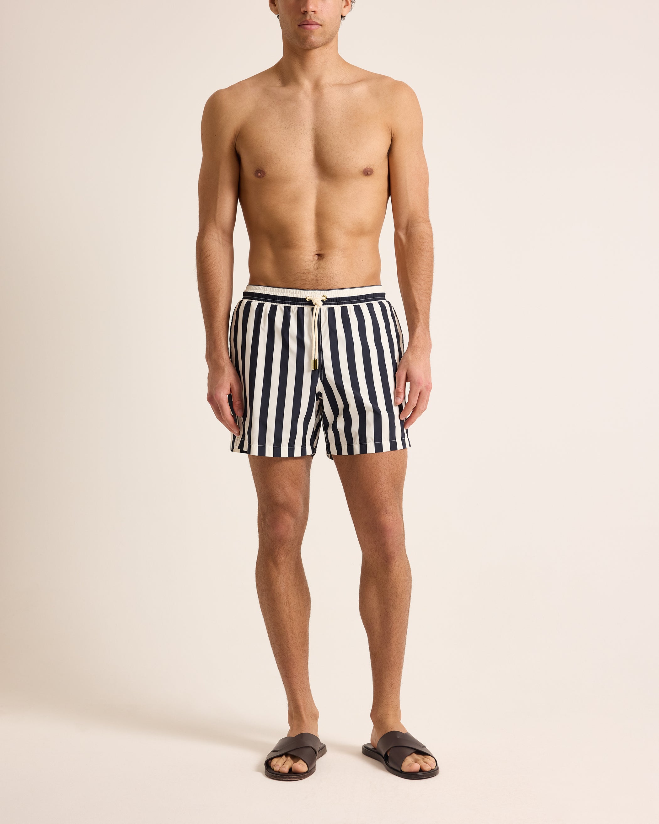Man wearing black and white striped swim shorts on a beige background