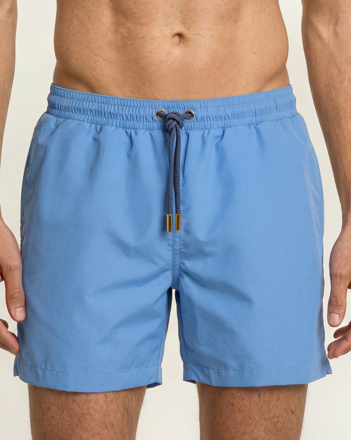 Closeup of bright blue swim shorts with gold detailing on drawstring. on a plain background