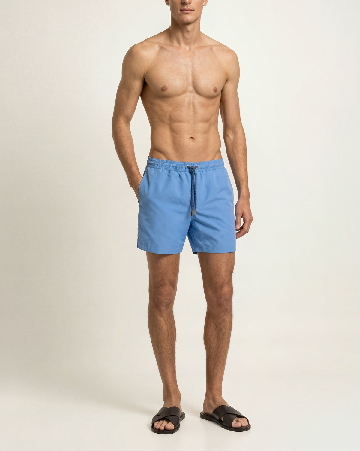 Man wearing bright blue swim short with drawcord waist and brown sandals on a plain background