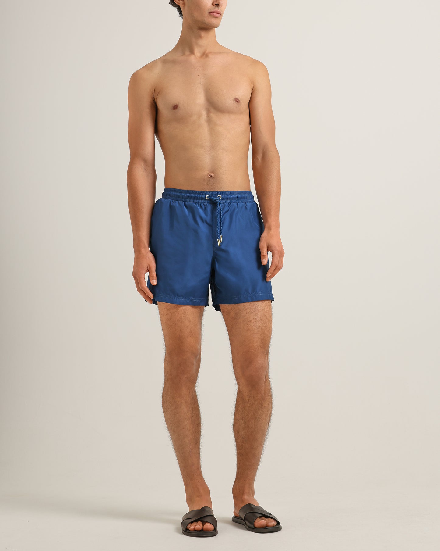 Man wearing blue swim shorts on a plain background